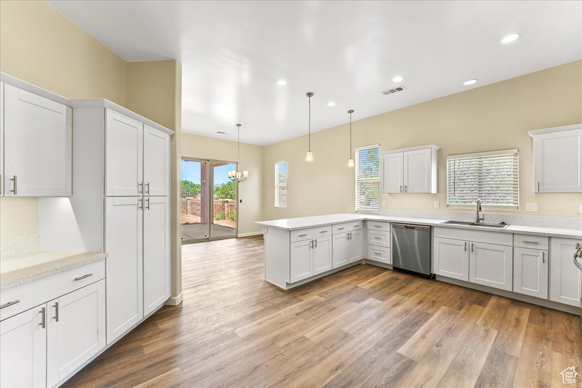 Kitchen featuring light hardwood / wood-style floors, stainless steel dishwasher, kitchen peninsula, decorative light fixtures, and sink