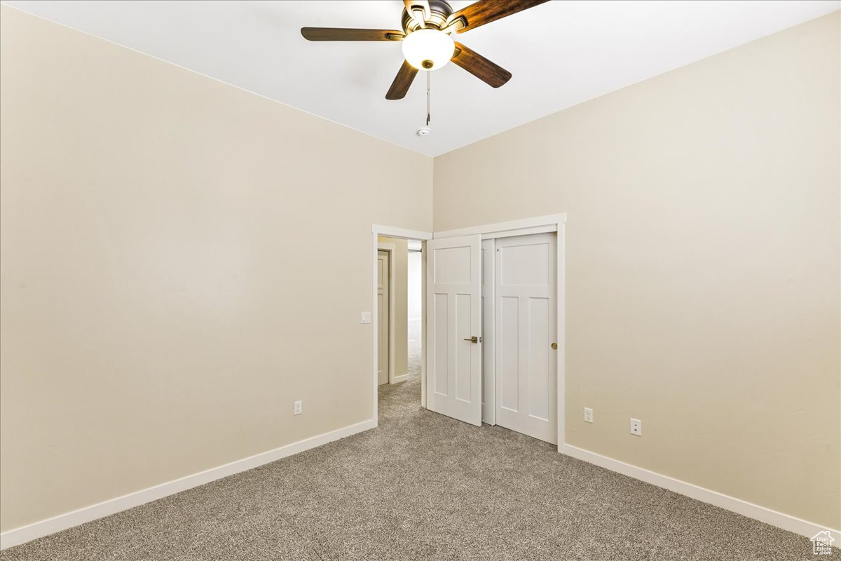 Carpeted empty room featuring ceiling fan and a towering ceiling