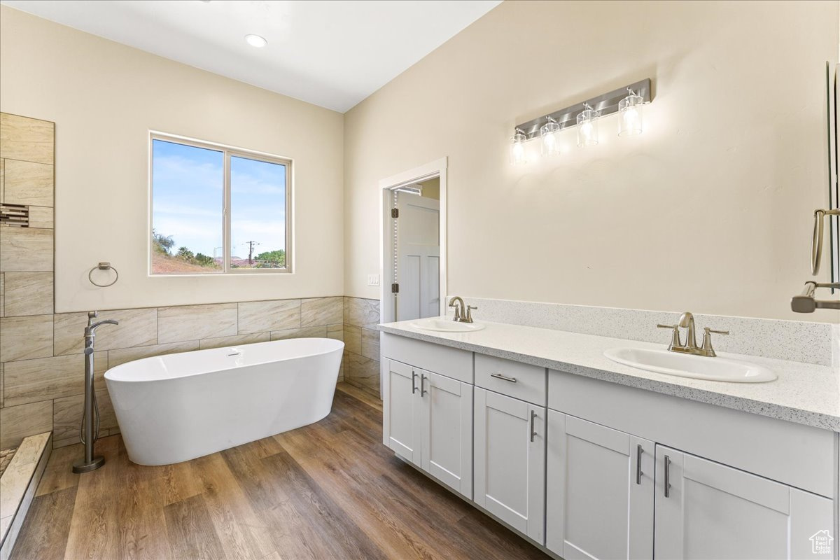 Bathroom with wood-type flooring, dual vanity, tile walls, and a bathing tub