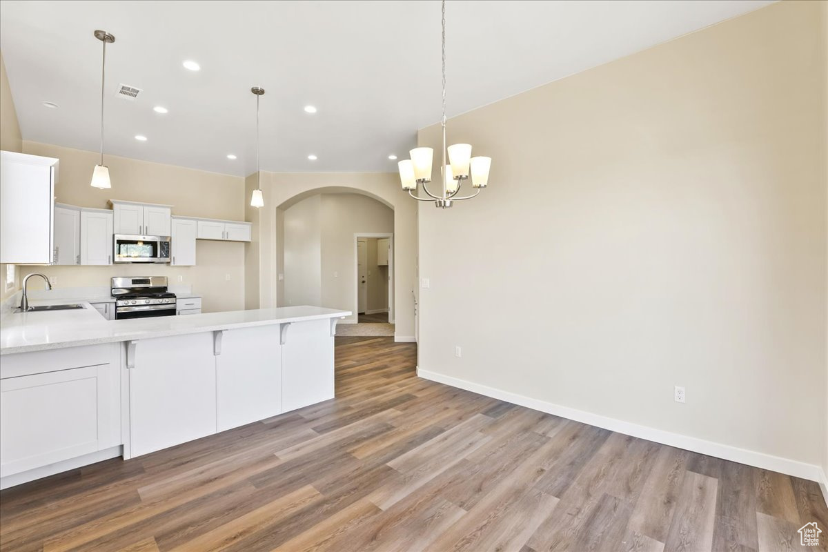 Kitchen featuring stainless steel appliances, pendant lighting, sink, white cabinets, and hardwood / wood-style flooring