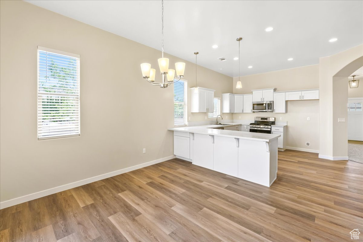 Kitchen with white cabinetry, hanging light fixtures, light hardwood / wood-style flooring, appliances with stainless steel finishes, and kitchen peninsula