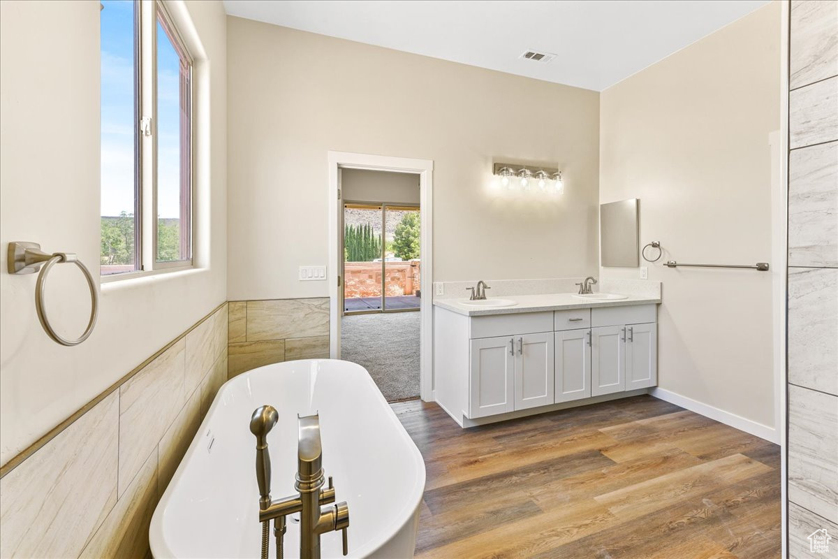 Bathroom with a healthy amount of sunlight, dual bowl vanity, wood-type flooring, and a bath to relax in