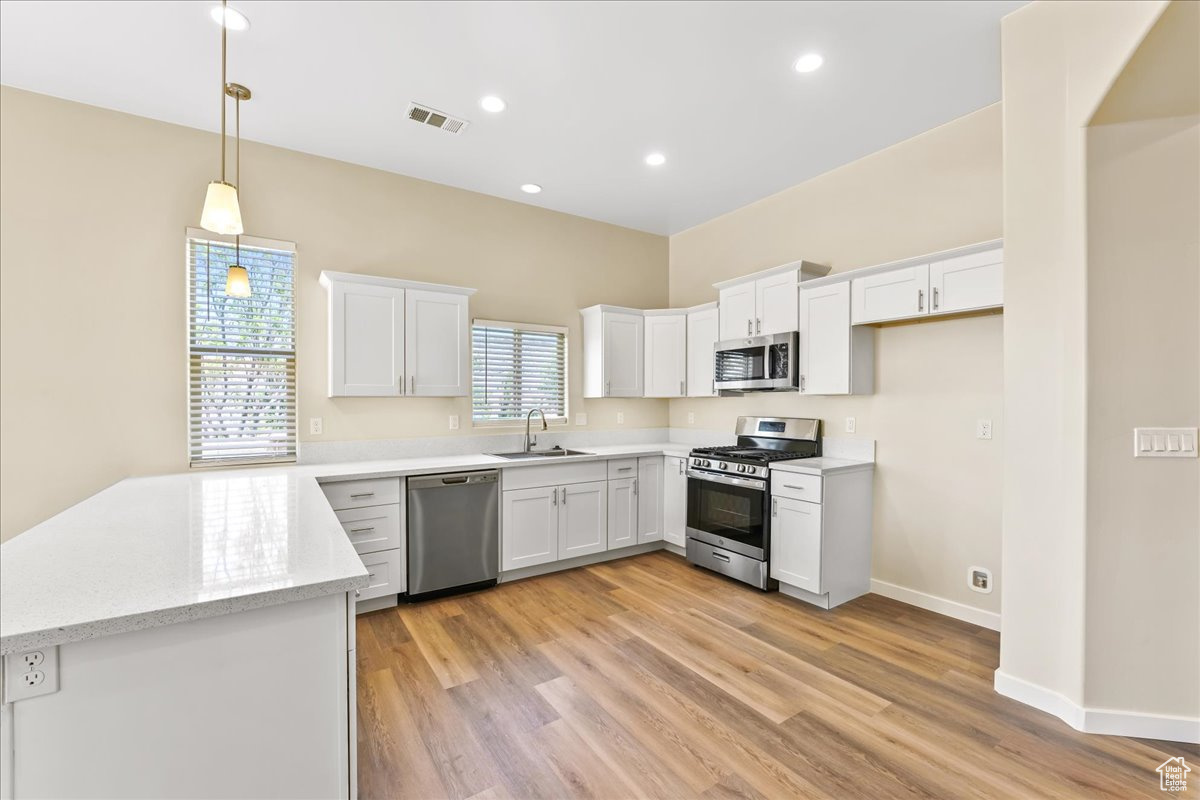 Kitchen featuring light hardwood / wood-style floors, stainless steel appliances, hanging light fixtures, sink, and white cabinets