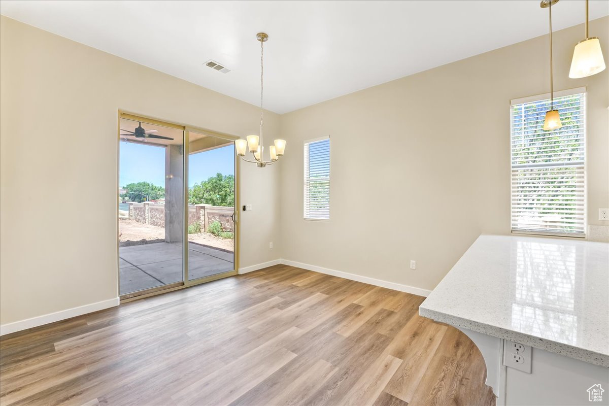 Unfurnished dining area featuring a wealth of natural light, wood-type flooring, and ceiling fan with notable chandelier