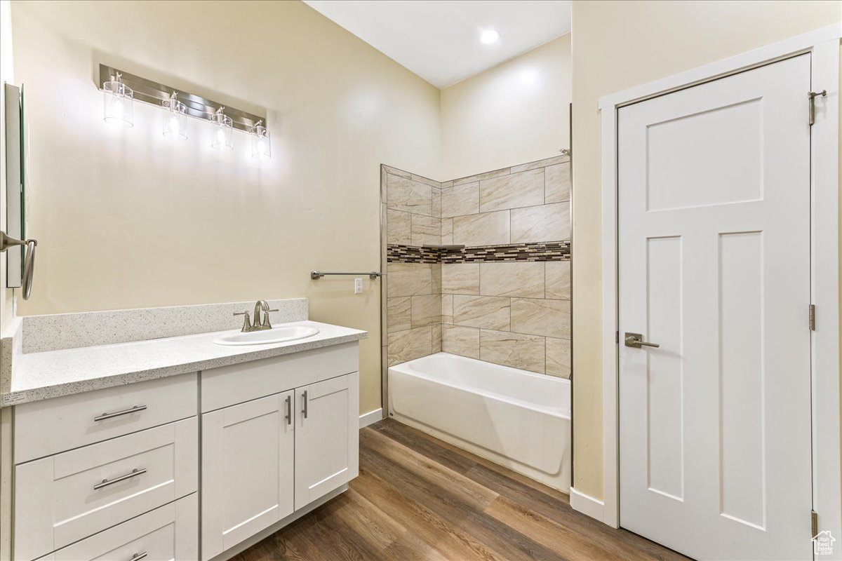 Bathroom with tiled shower / bath combo, hardwood / wood-style flooring, and vanity