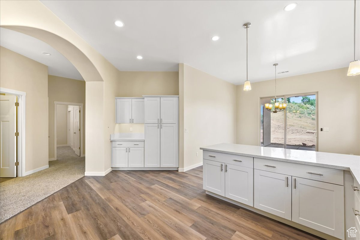 Kitchen featuring white cabinetry, a notable chandelier, pendant lighting, and wood-type flooring