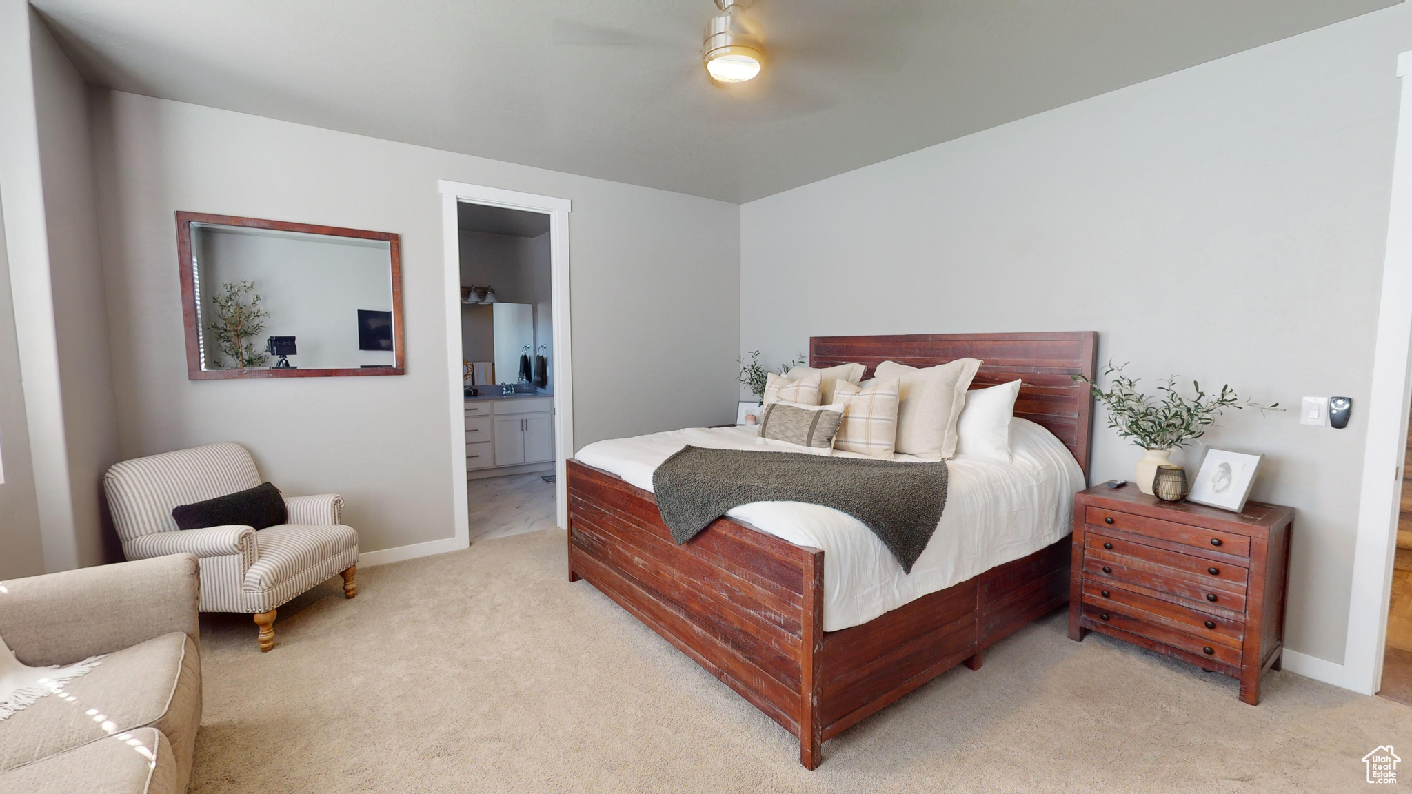 Carpeted primary main floor bedroom featuring ensuite bathroom and ceiling fan