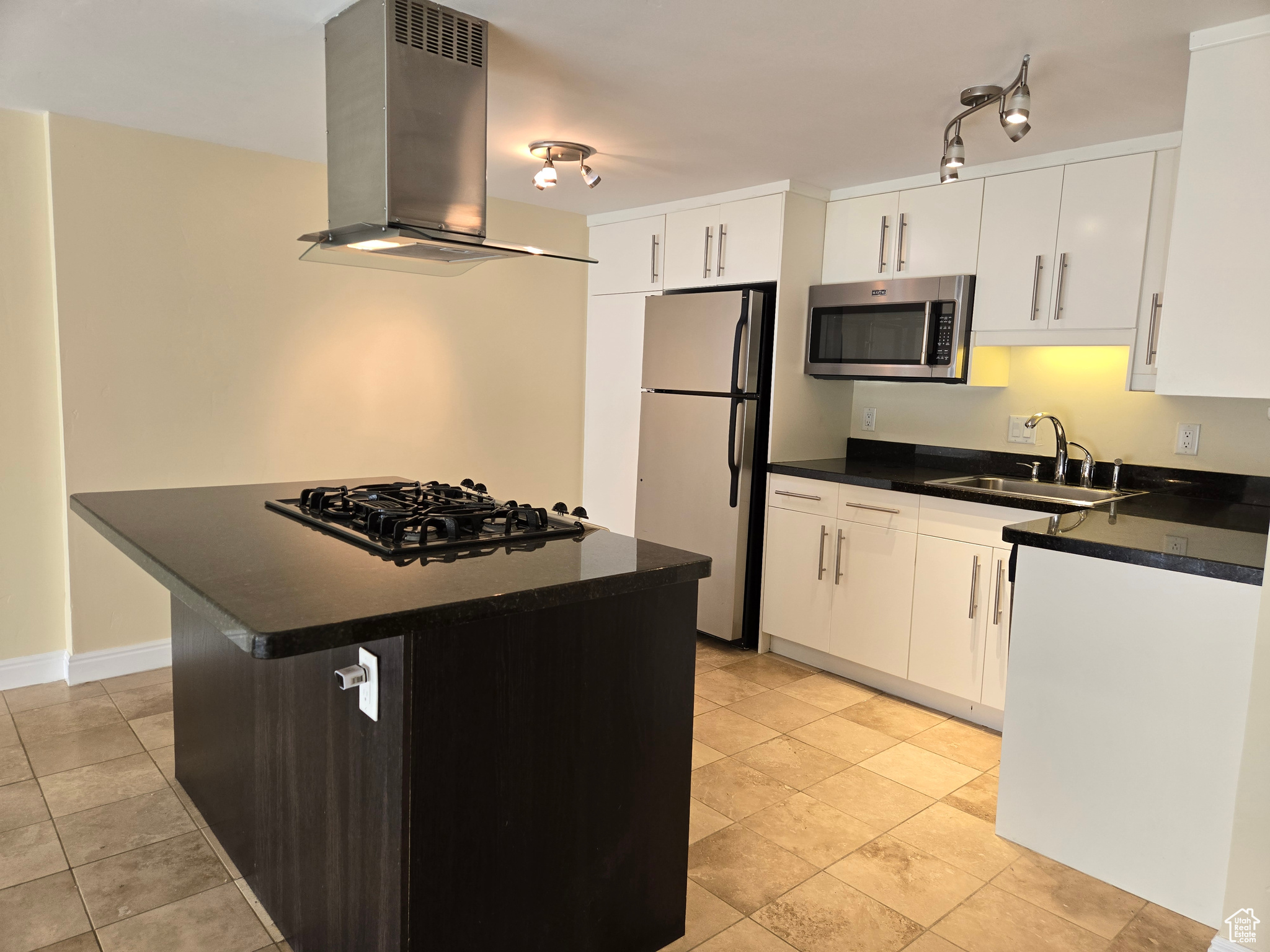 Kitchen with white cabinets, wall chimney range hood, stainless steel appliances, sink, and light tile floors