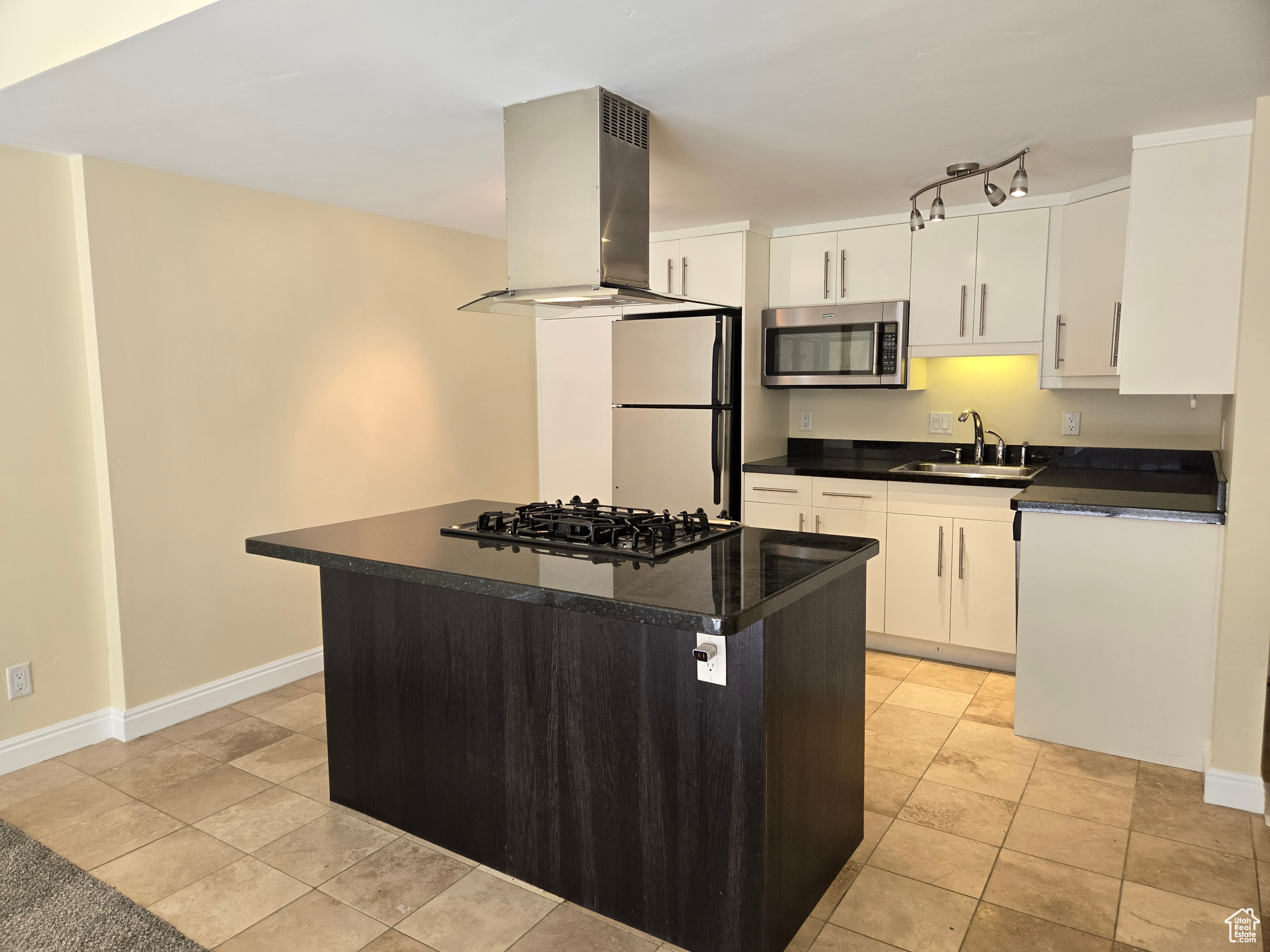 Kitchen featuring refrigerator, white cabinets, black gas stovetop, and range hood