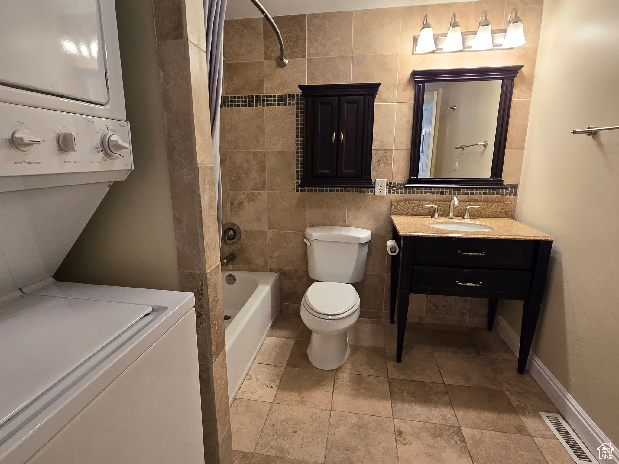 Full bathroom featuring shower / tub combination, tile floors, stacked washer and dryer, tile walls, and vanity