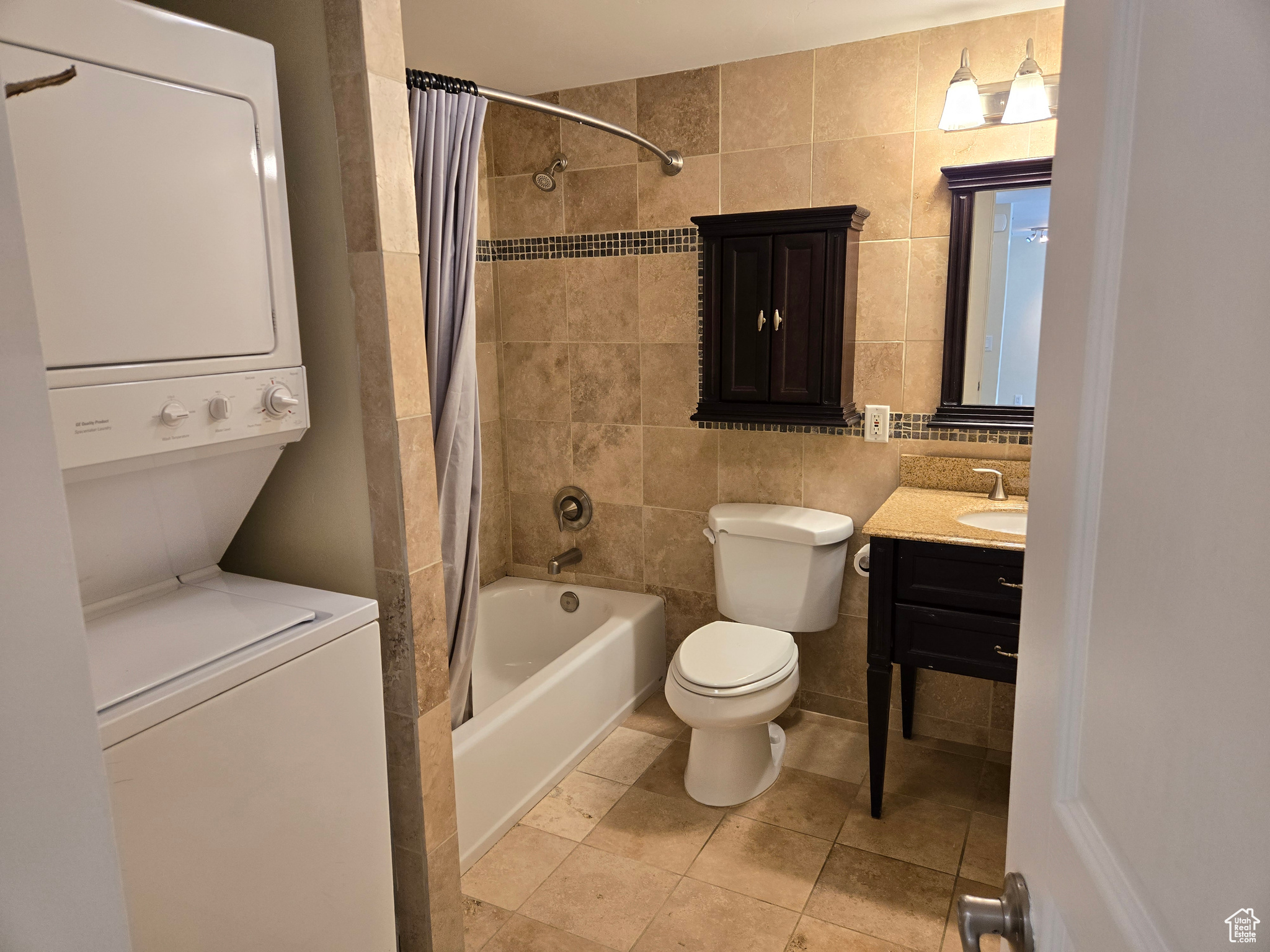 Full bathroom with stacked washer and dryer, shower / tub combo with curtain, vanity, and tile walls