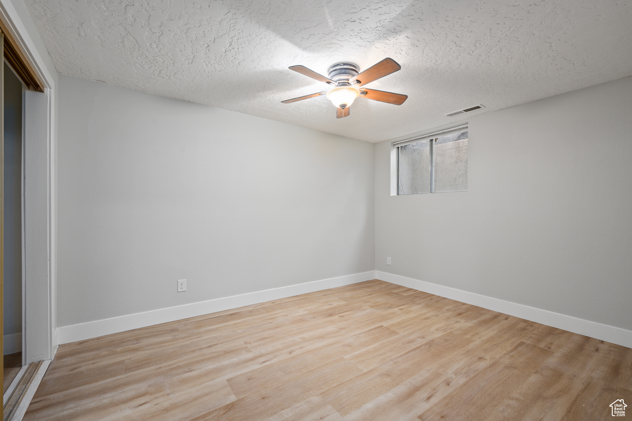 Unfurnished room with ceiling fan, a textured ceiling, and light wood-type flooring