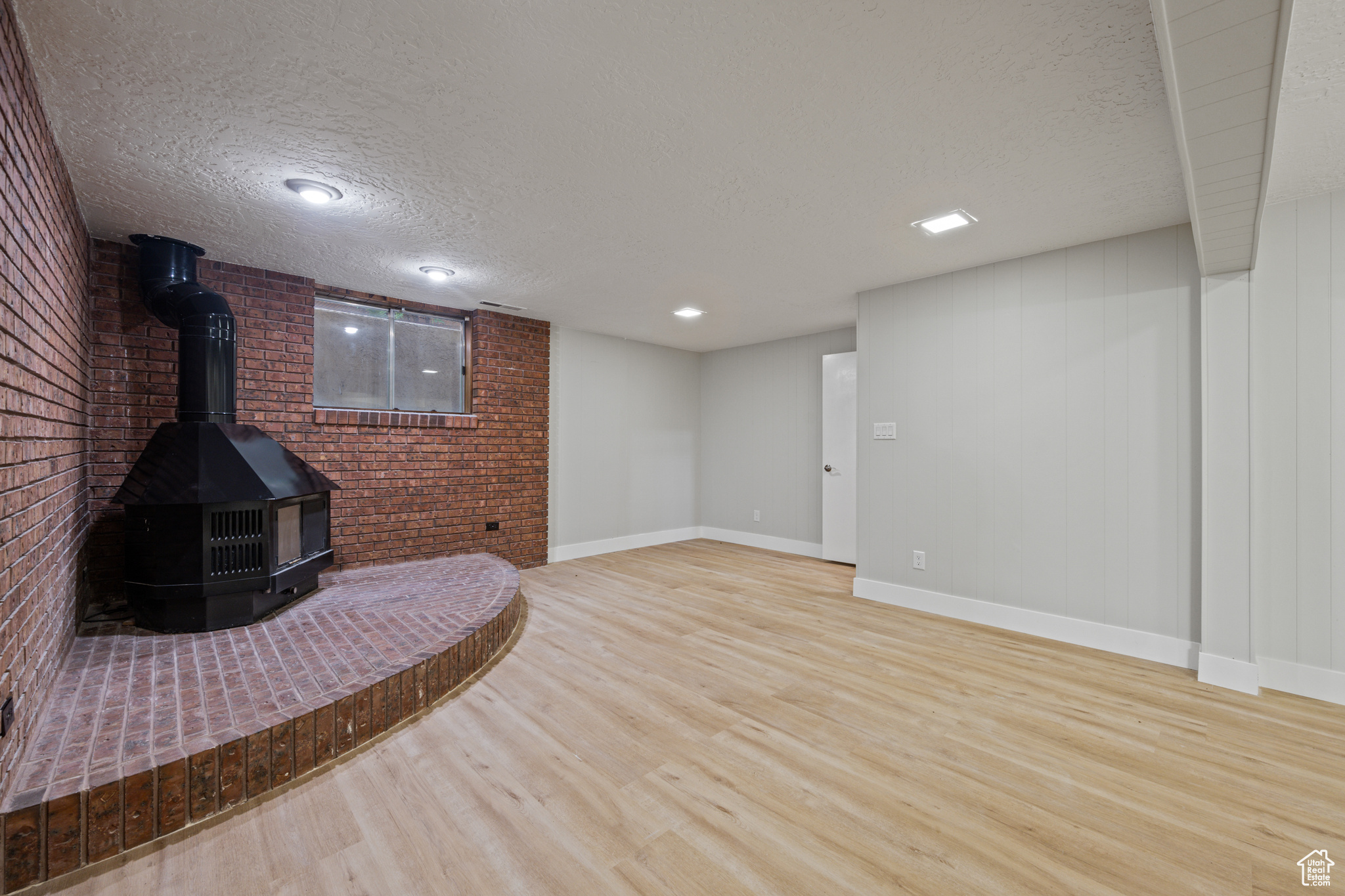 Unfurnished living room featuring a textured ceiling, light wood-type flooring, and a wood stove