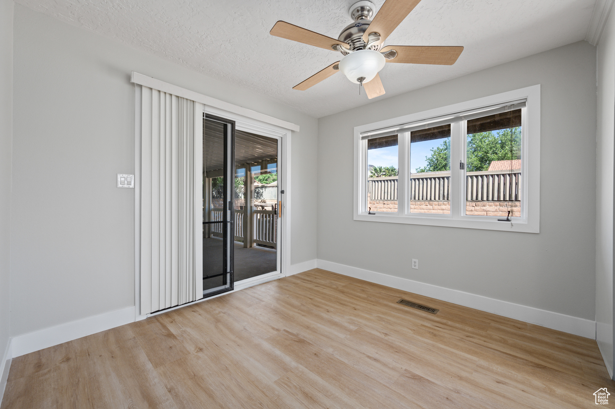 Empty room with a textured ceiling, light wood-type flooring, and ceiling fan