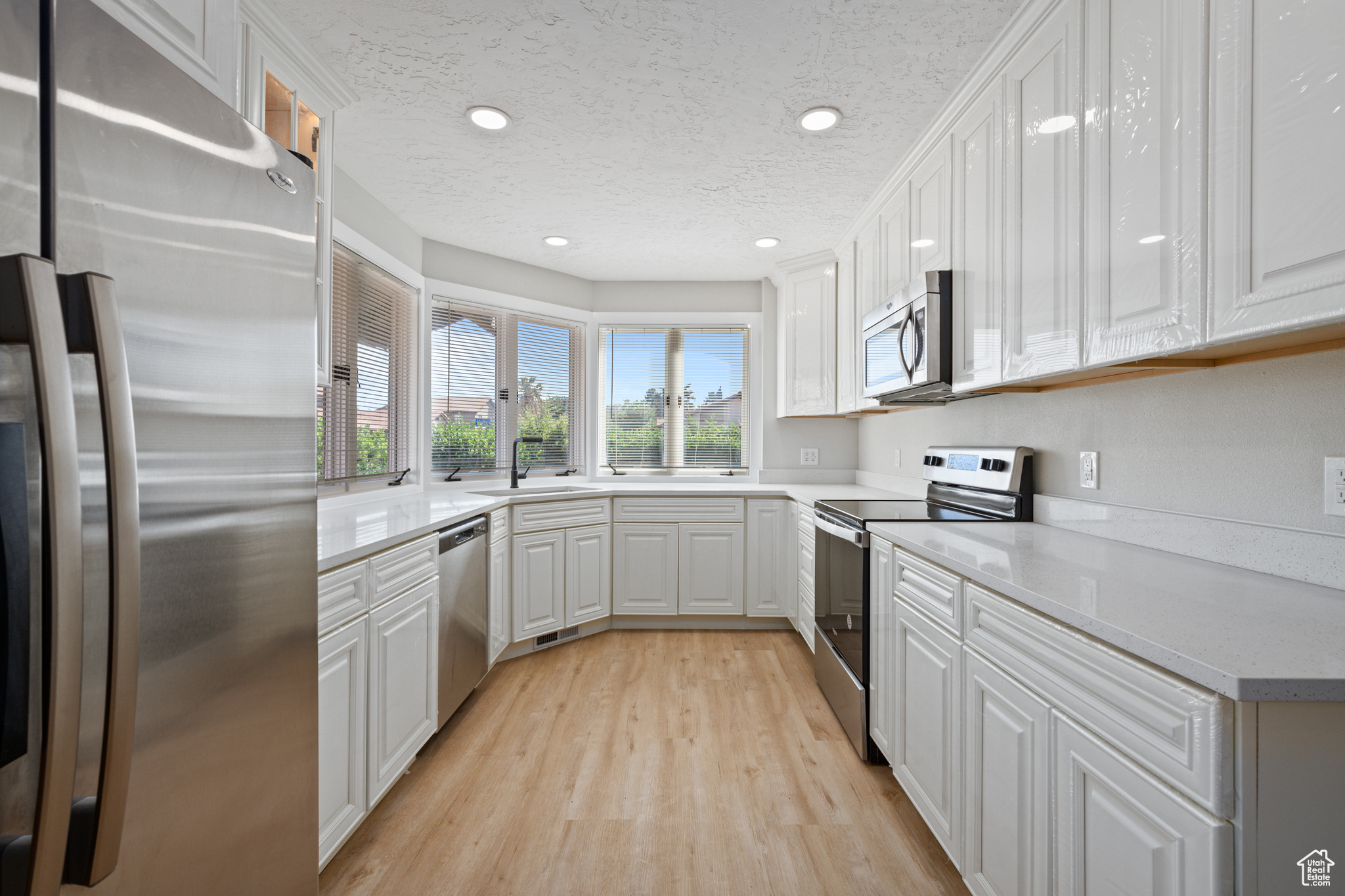 Kitchen with stainless steel appliances, light wood-type flooring, a textured ceiling, sink, and white cabinets