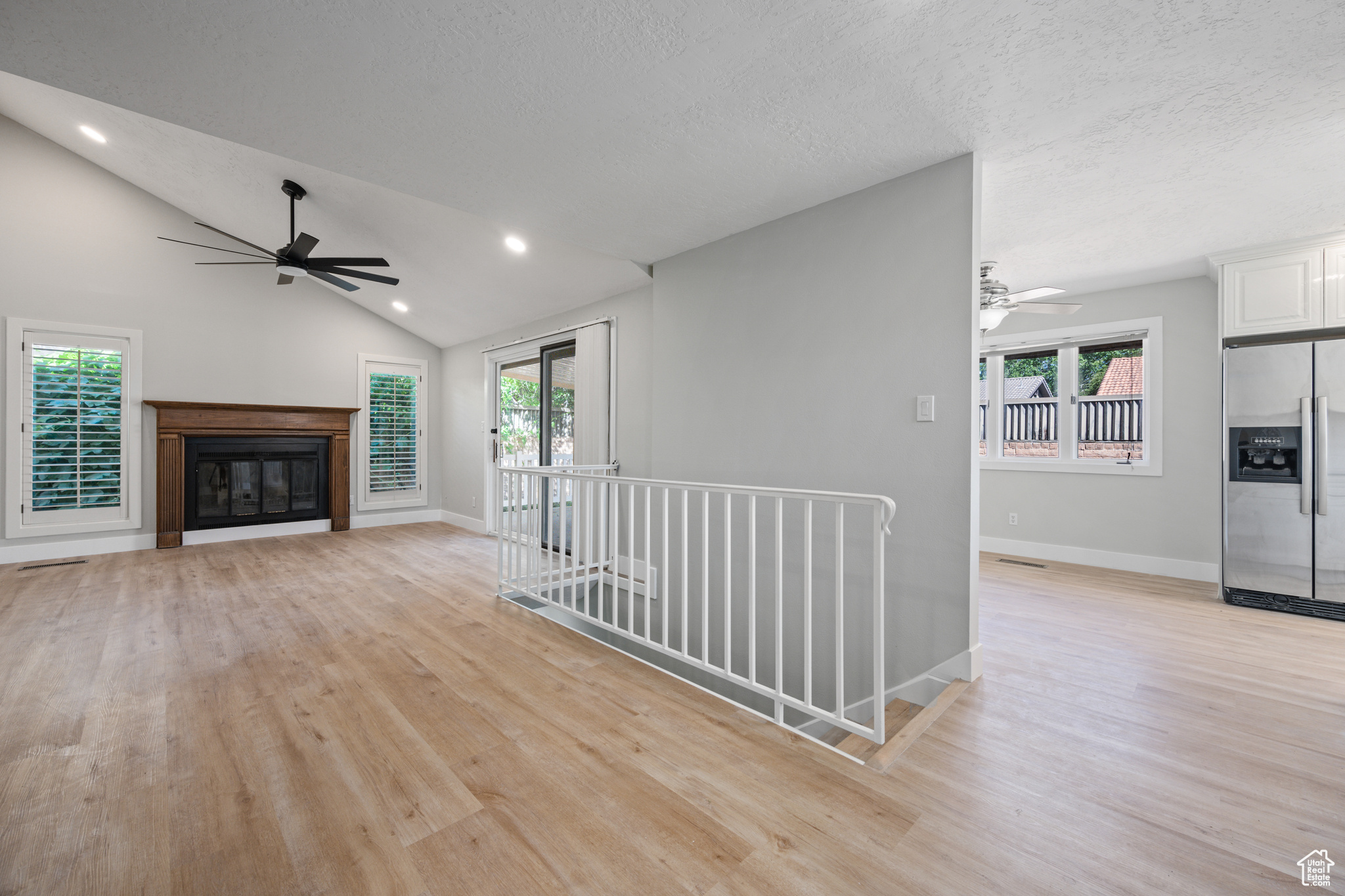 Unfurnished living room with ceiling fan, vaulted ceiling, and light wood-type flooring