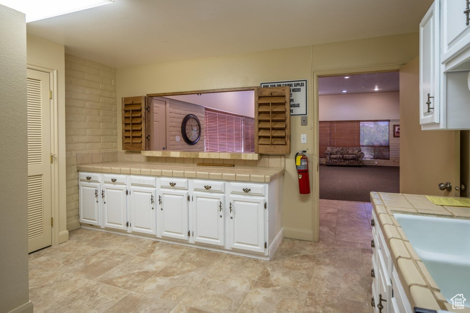 Kitchen featuring tile countertops, sink, and white cabinets