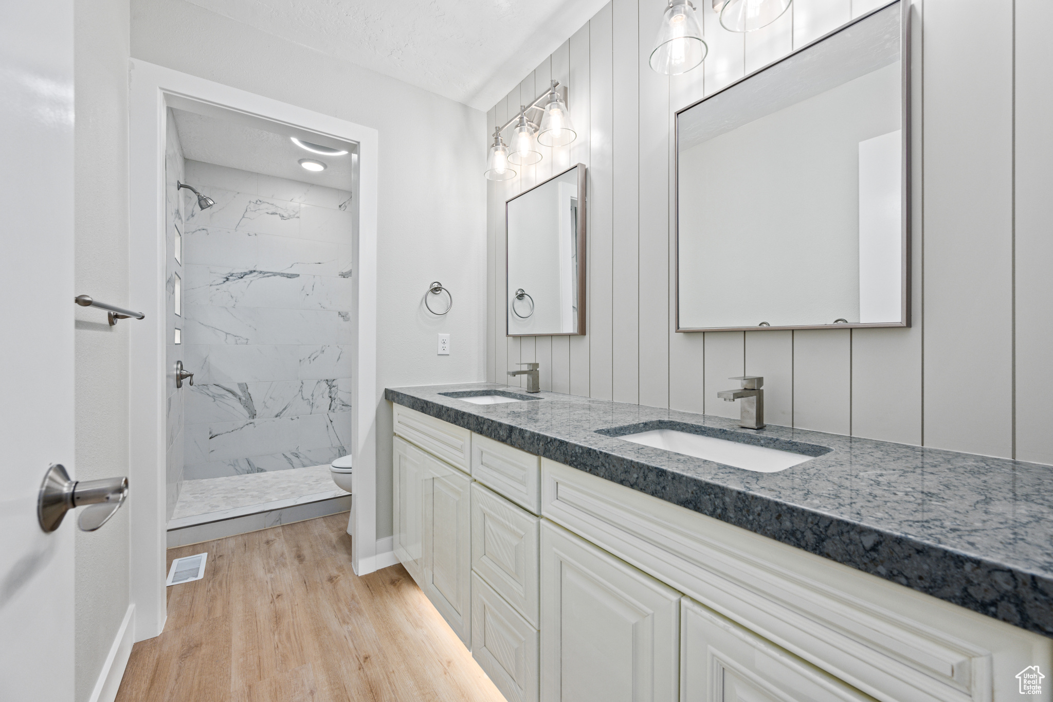 Bathroom with tiled shower, hardwood / wood-style floors, dual vanity, and toilet