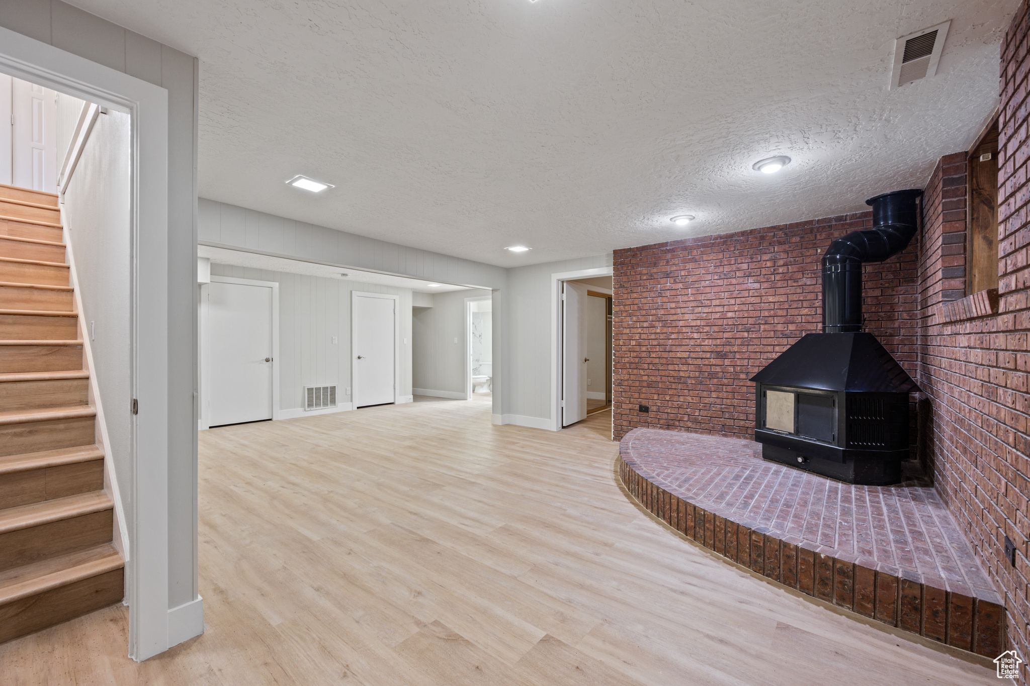 Unfurnished living room featuring light hardwood / wood-style floors, a textured ceiling, brick wall, and a wood stove