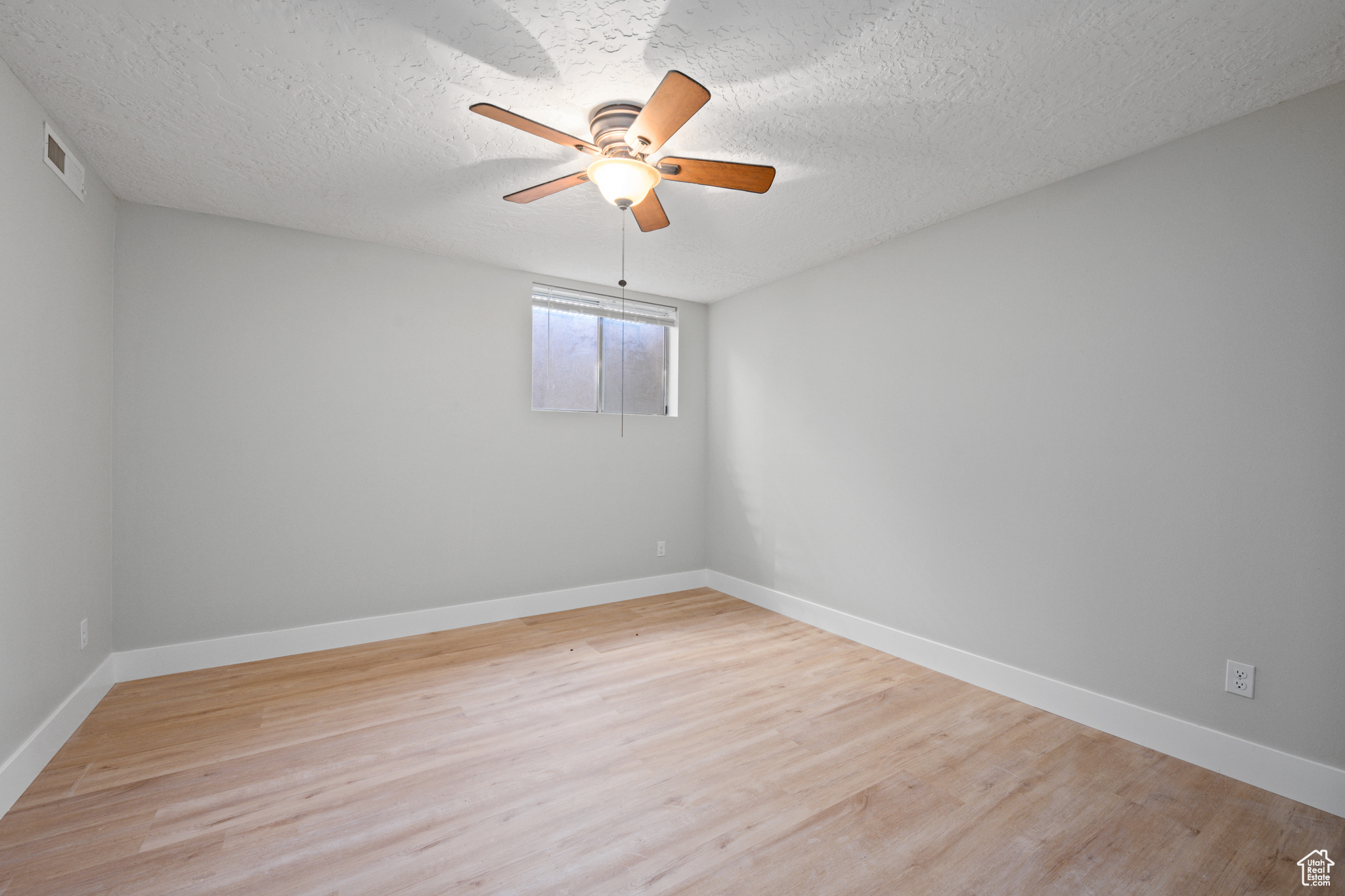 Unfurnished room with a textured ceiling, light wood-type flooring, and ceiling fan