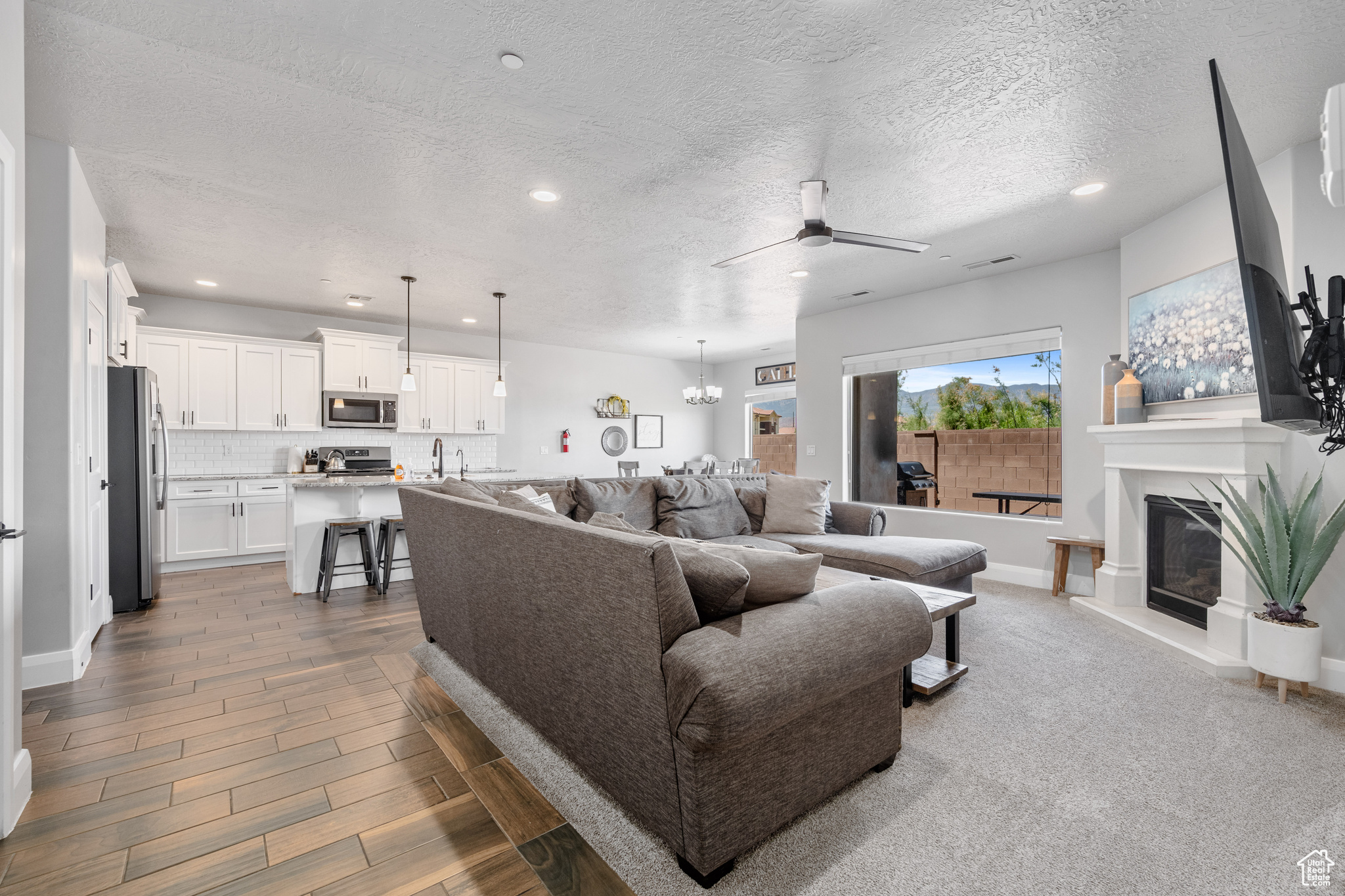 Carpeted living room featuring a high end fireplace, ceiling fan with notable chandelier, a textured ceiling, and sink