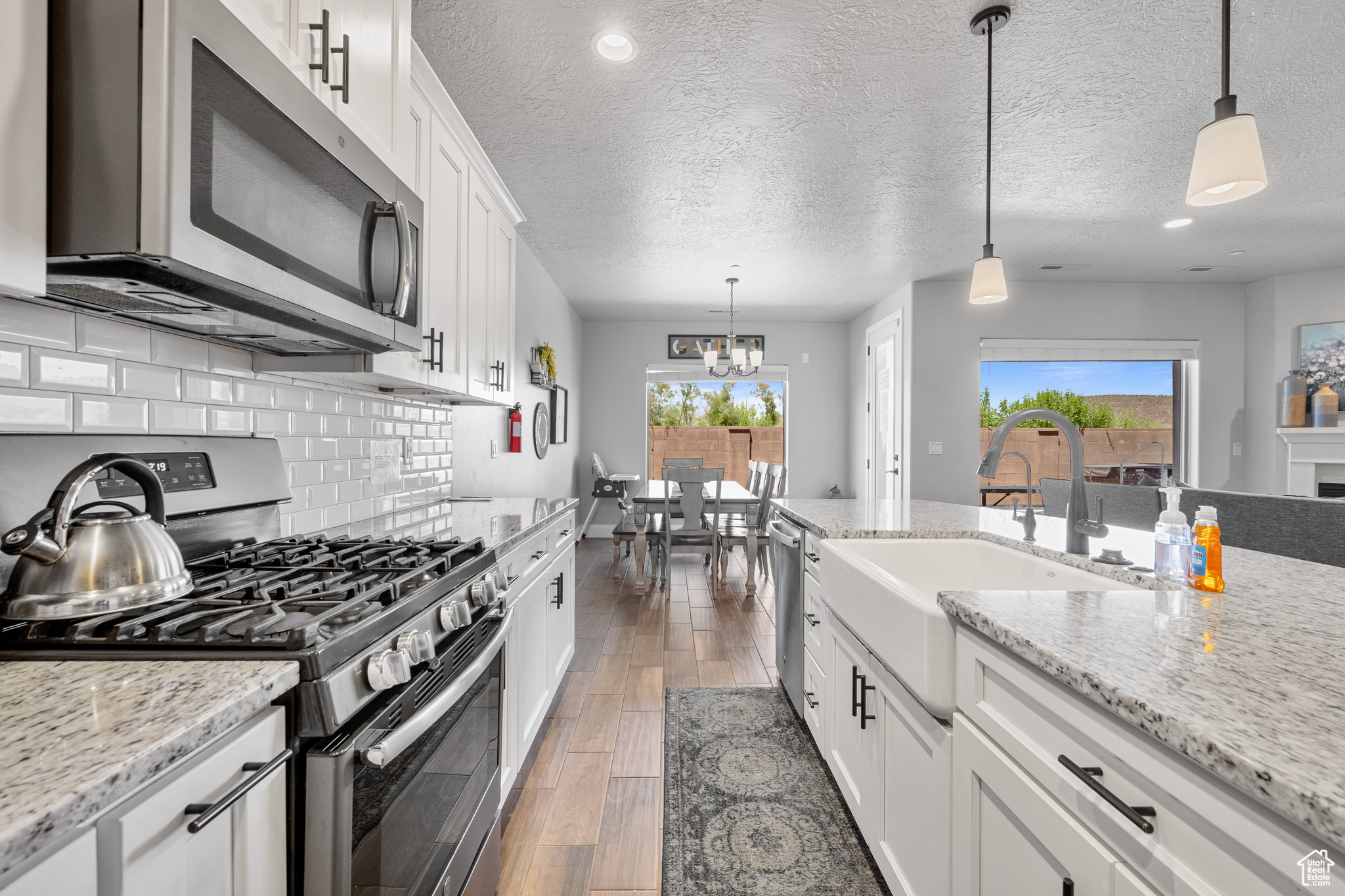 Kitchen featuring hanging light fixtures, appliances with stainless steel finishes, white cabinets, backsplash, and wood-type flooring