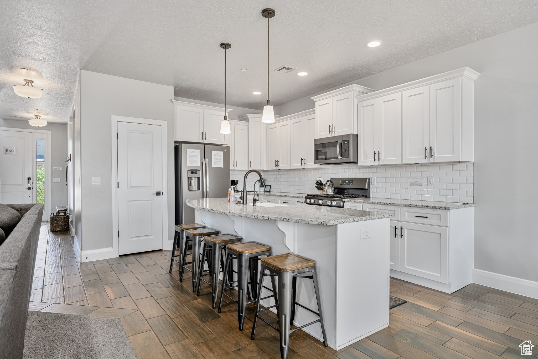 Kitchen featuring backsplash, appliances with stainless steel finishes, white cabinetry, and a kitchen island with sink