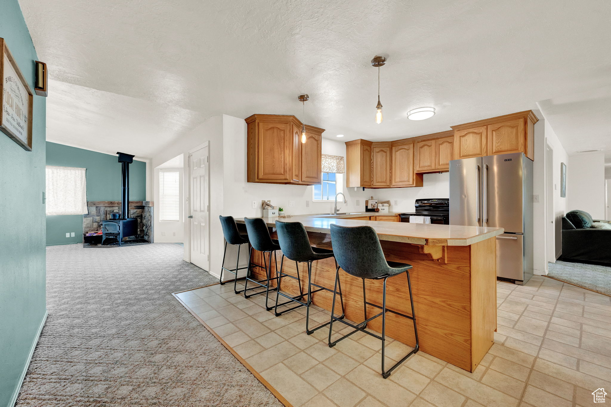 Kitchen featuring light carpet, a wood stove, range with electric cooktop, and a kitchen breakfast bar