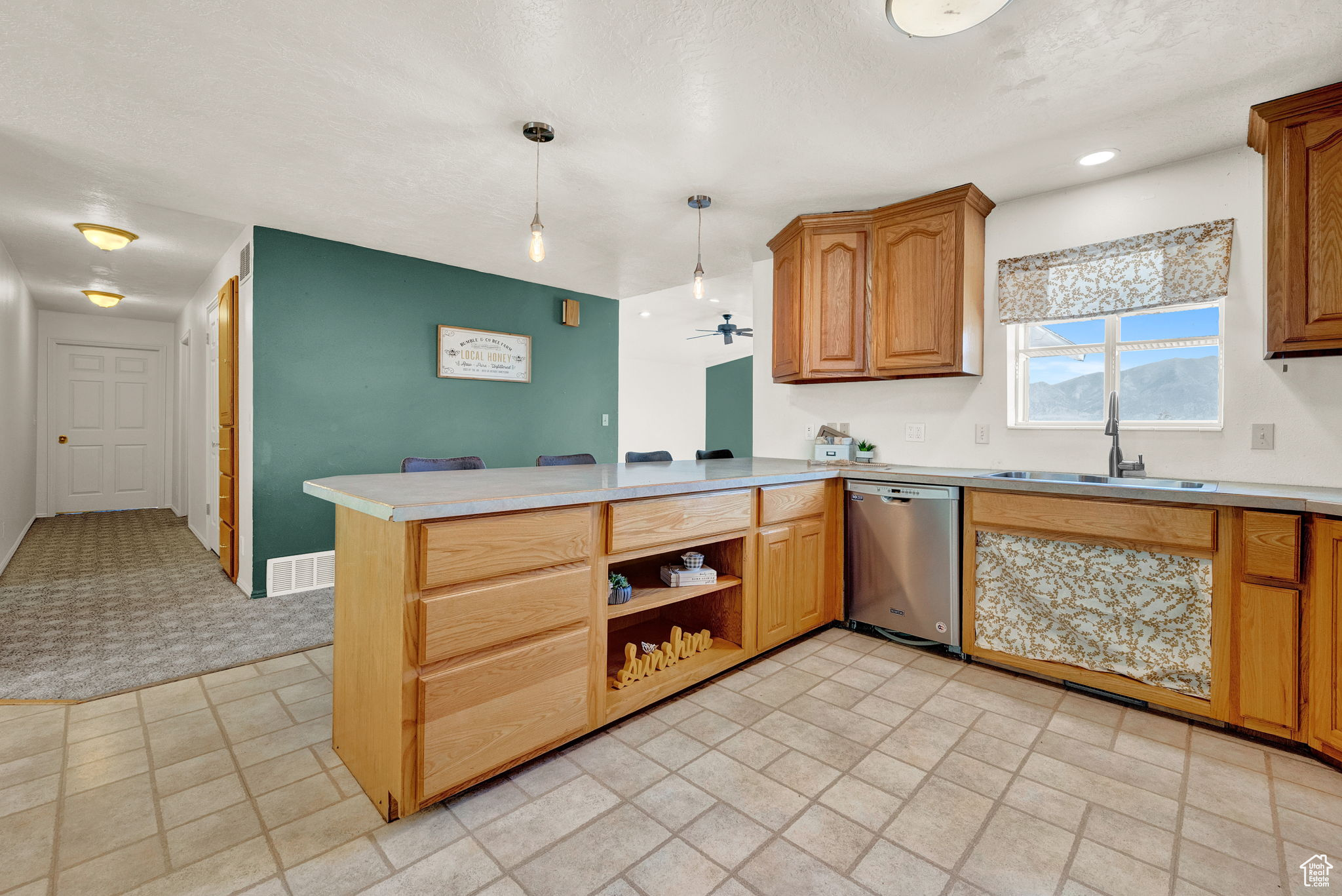 Kitchen with stainless steel dishwasher, light tile patterned floors, hanging light fixtures, sink, and kitchen peninsula