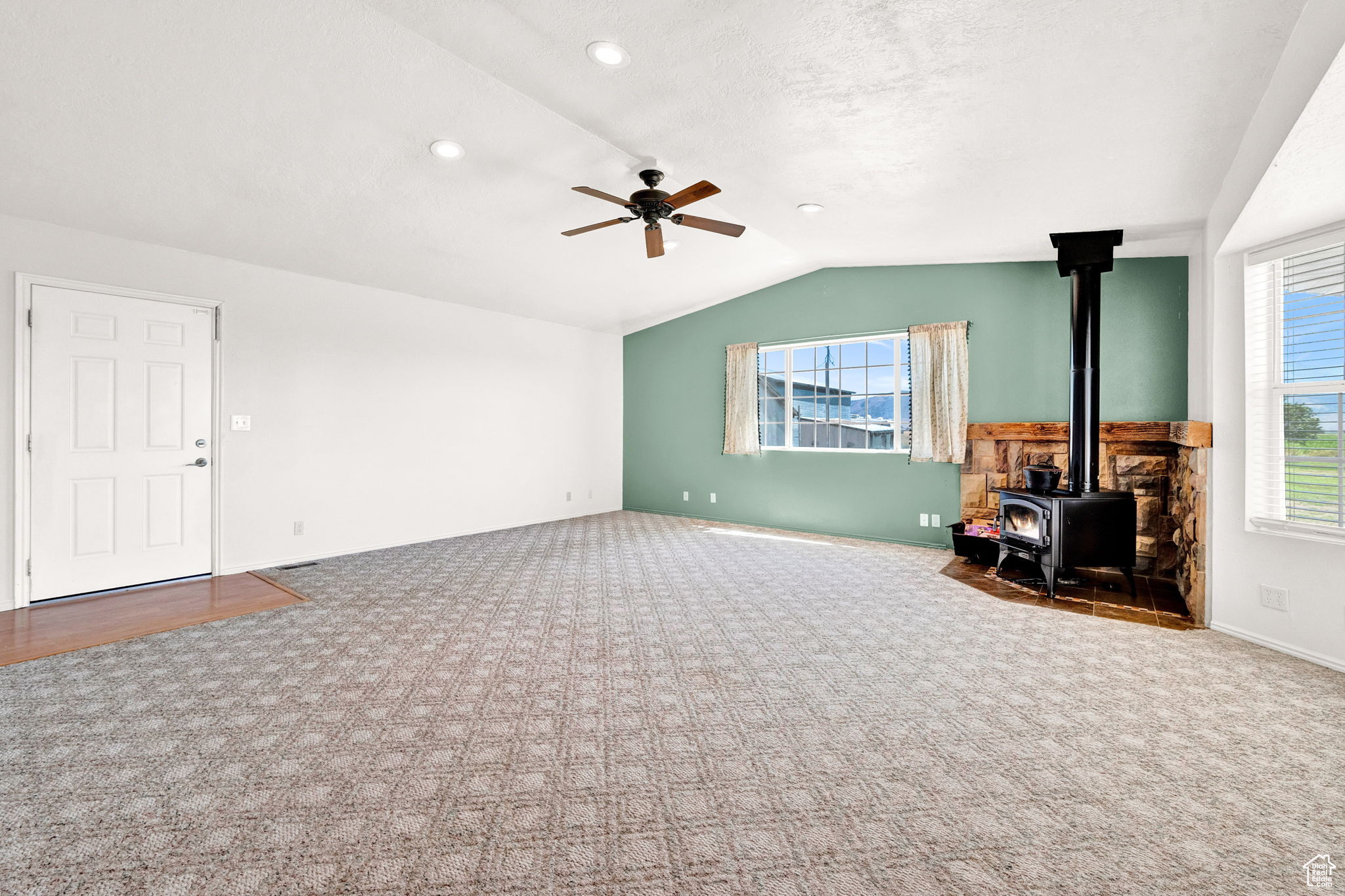 Unfurnished living room featuring a wood stove, a healthy amount of sunlight, carpet floors, and ceiling fan