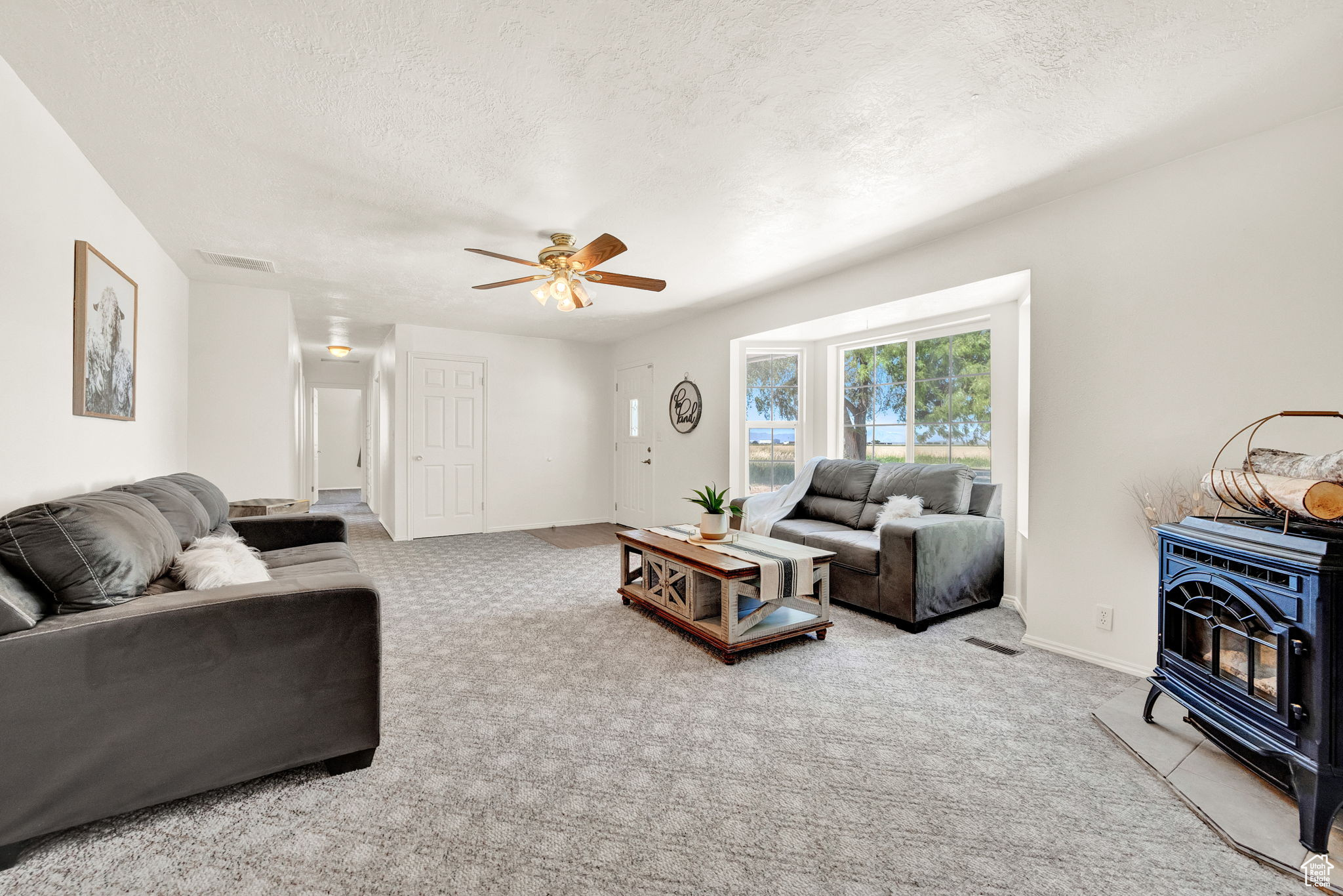 Living room with a wood stove, carpet floors, a textured ceiling, and ceiling fan