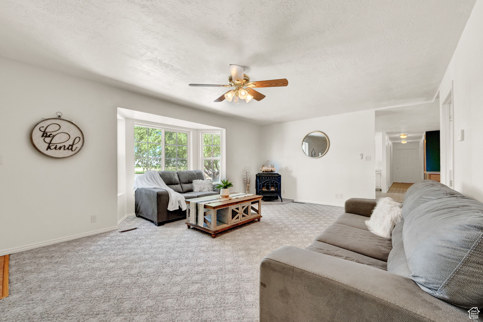 Living room featuring a textured ceiling, carpet, ceiling fan, and a wood stove