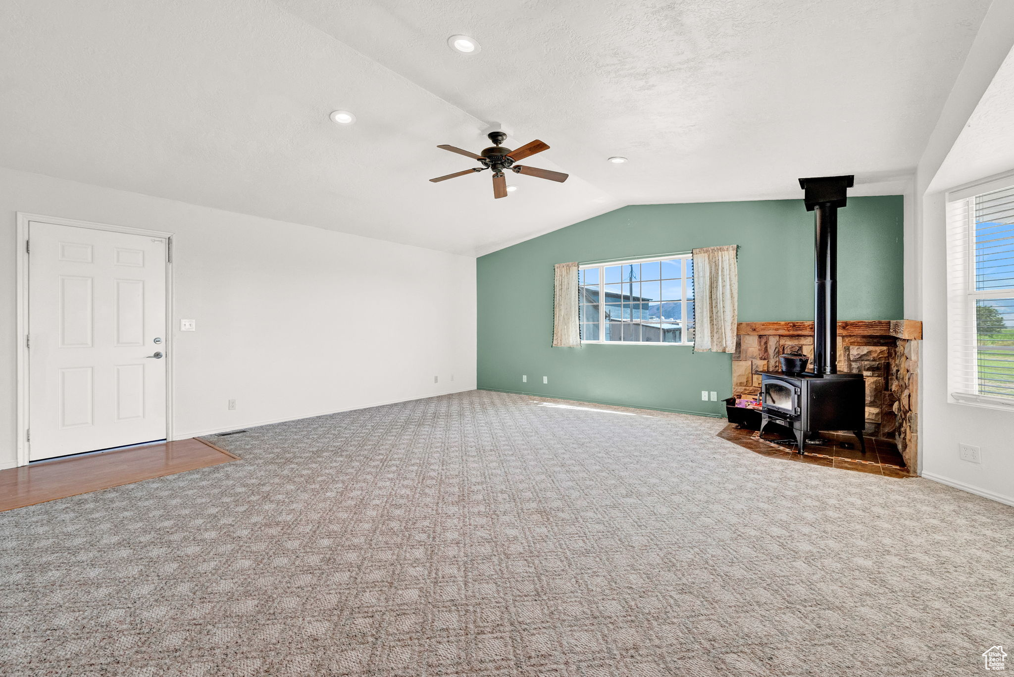 Unfurnished living room with a wood stove, carpet, ceiling fan, and plenty of natural light