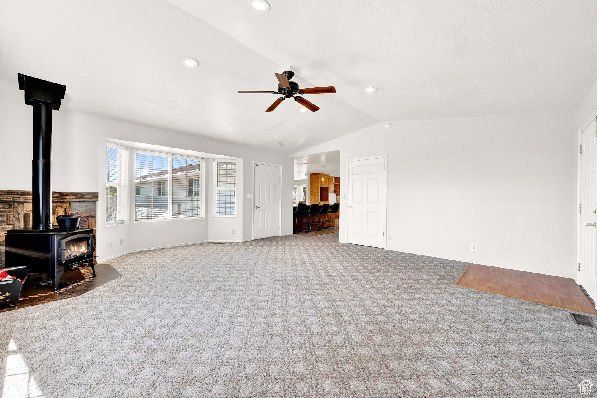 Carpeted living room with ceiling fan, lofted ceiling, and a wood stove