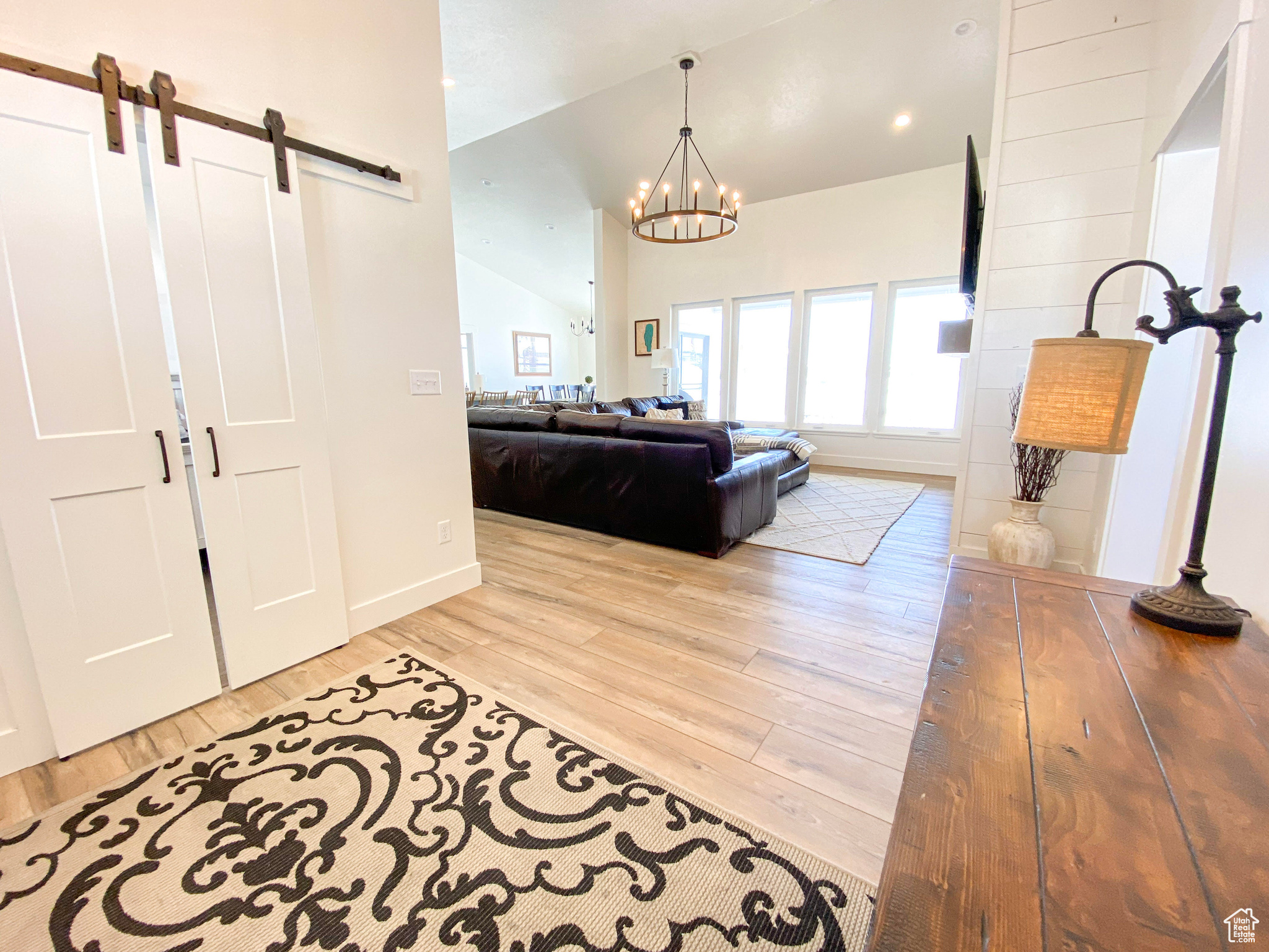 Living room with a barn door, a notable chandelier, hardwood / wood-style flooring, and lofted ceiling