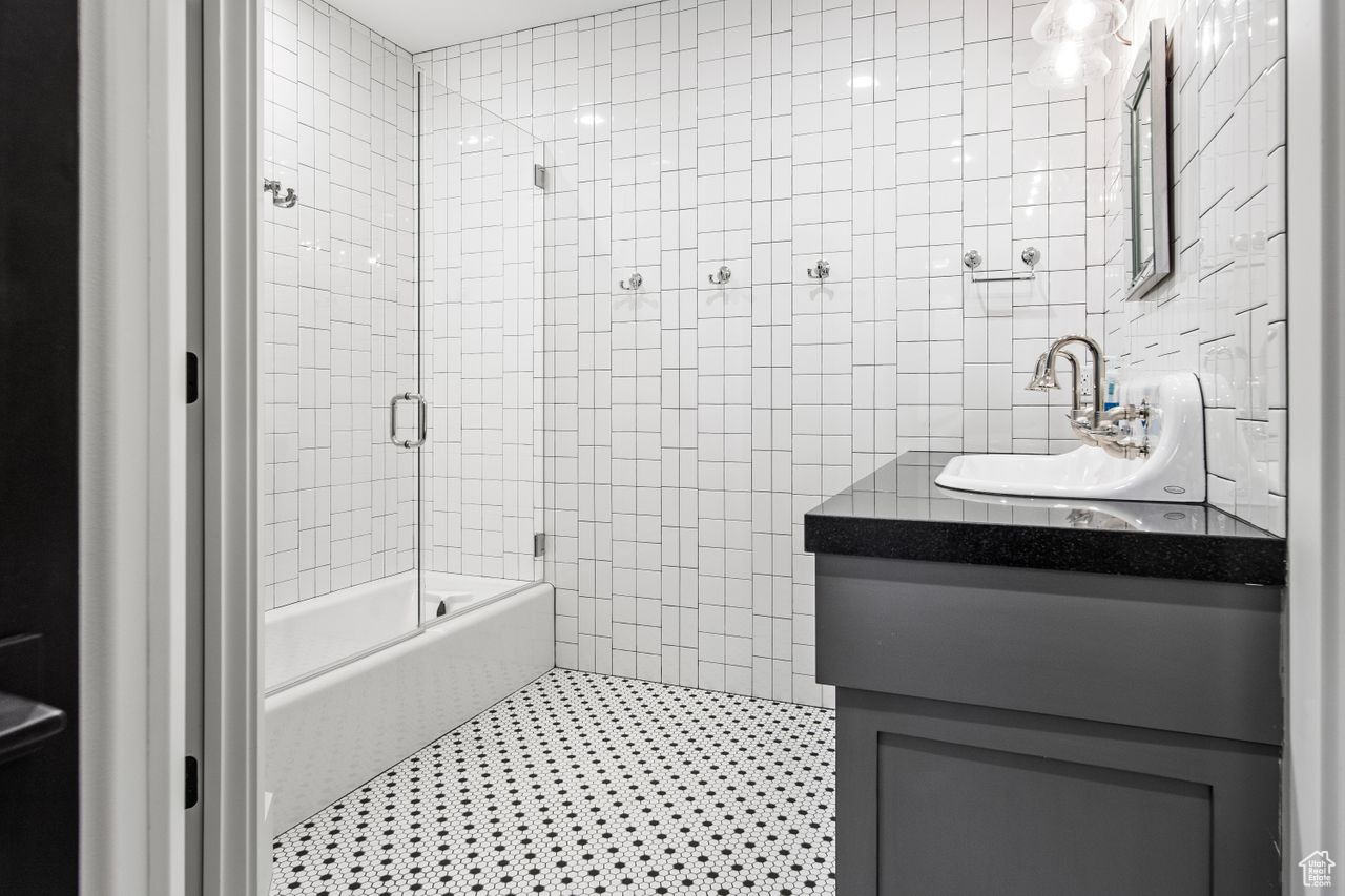 Bathroom featuring combined bath / shower with glass door, vanity, and tile walls