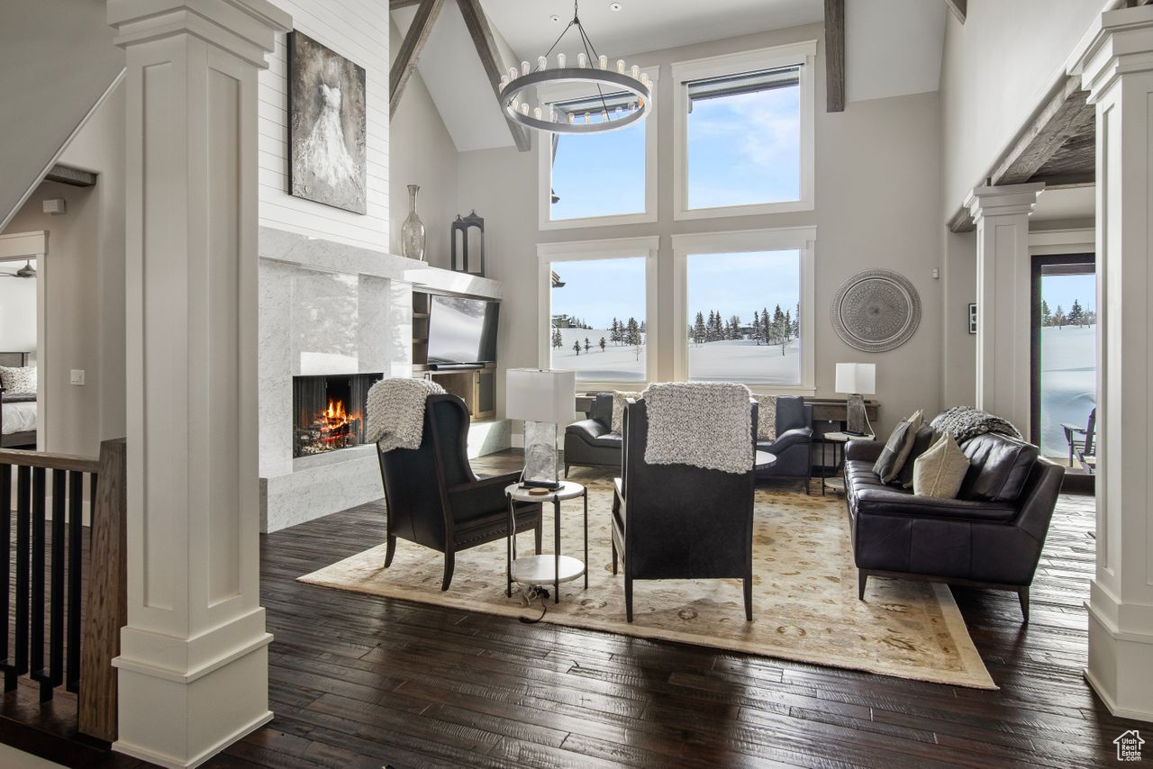 Living room featuring a fireplace, dark hardwood / wood-style floors, a chandelier, ornate columns, and high vaulted ceiling