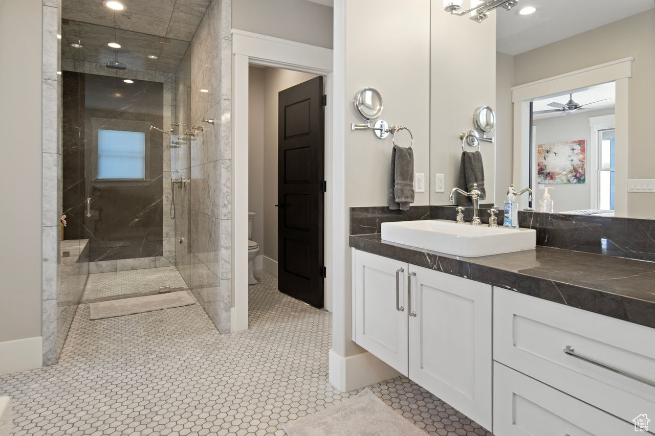 Bathroom featuring ceiling fan, toilet, a shower with shower door, tile flooring, and vanity