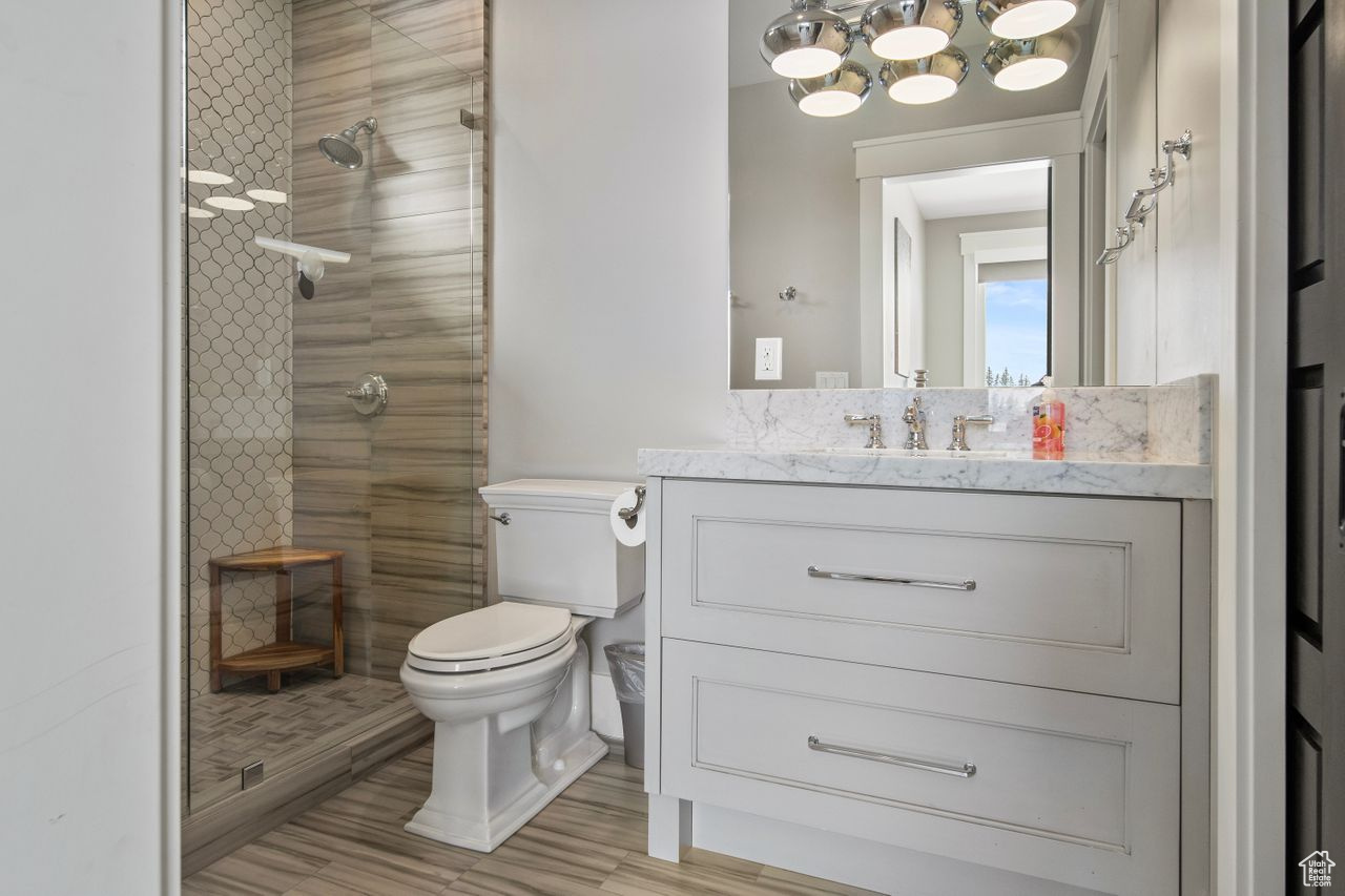 Bathroom with a tile shower, large vanity, a notable chandelier, and toilet