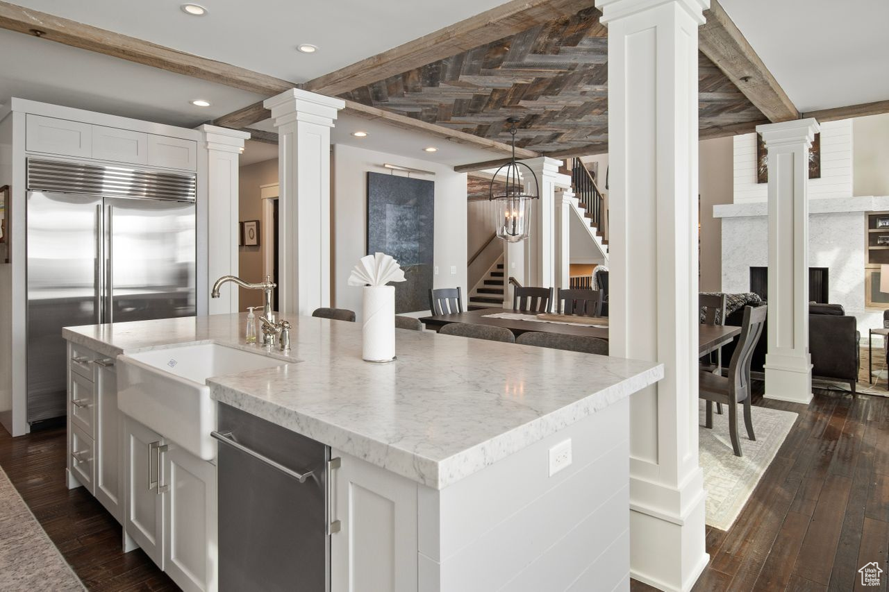 Kitchen featuring dark wood-type flooring, an island with sink, appliances with stainless steel finishes, white cabinets, and beam ceiling