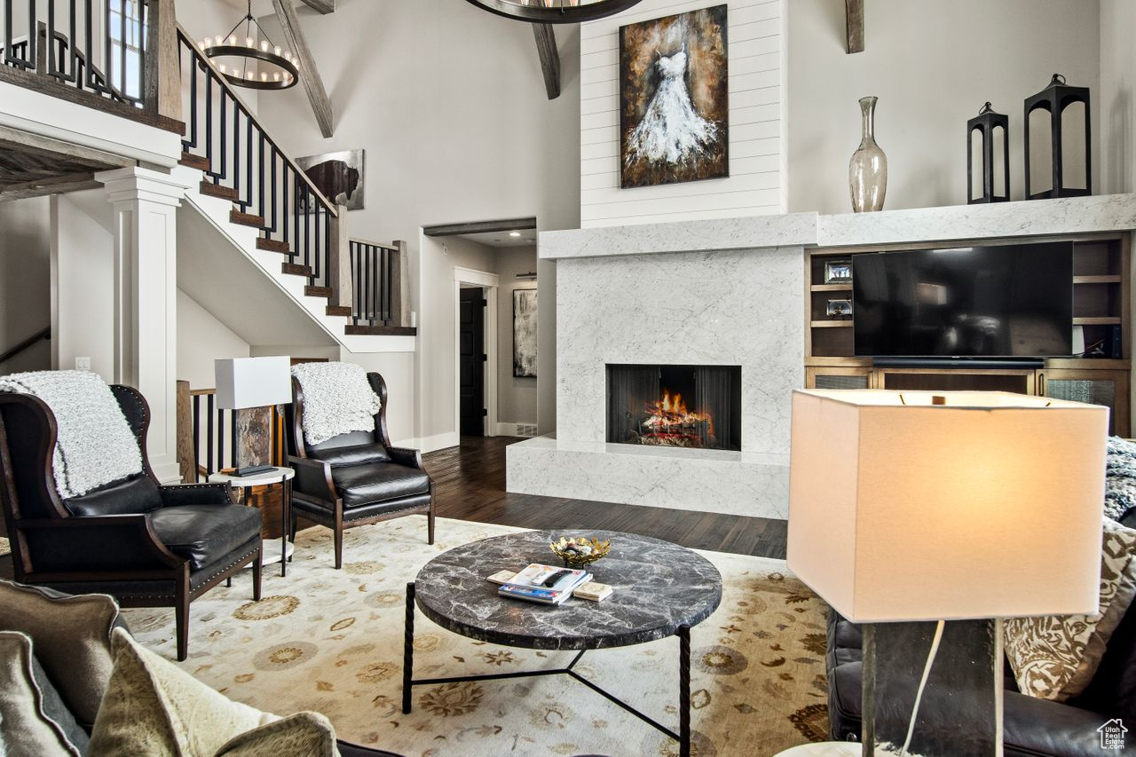 Living room with dark wood-type flooring, a fireplace, beamed ceiling, a high ceiling, and ornate columns