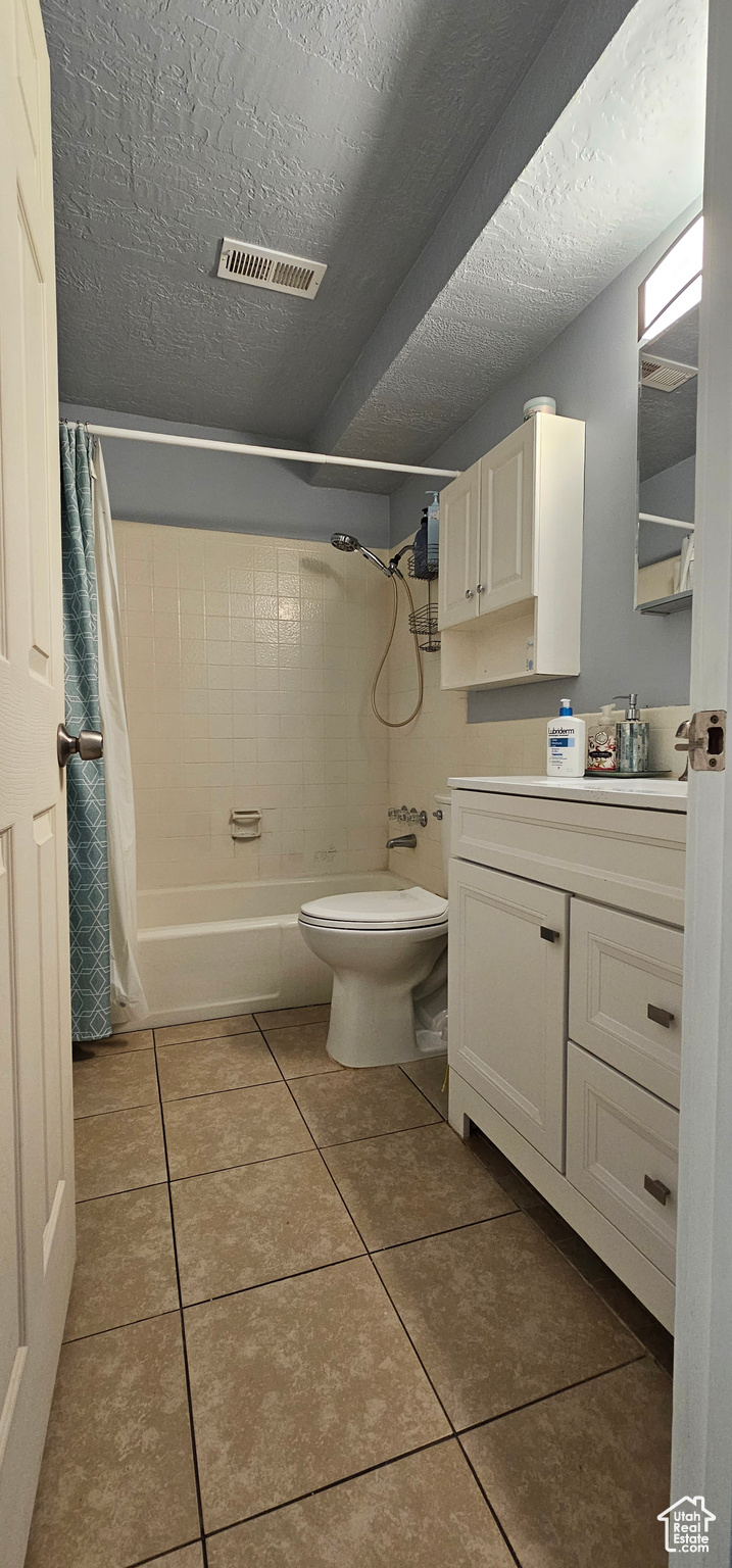 Full bathroom featuring toilet, tile floors, shower / bath combo with shower curtain, vanity, and a textured ceiling