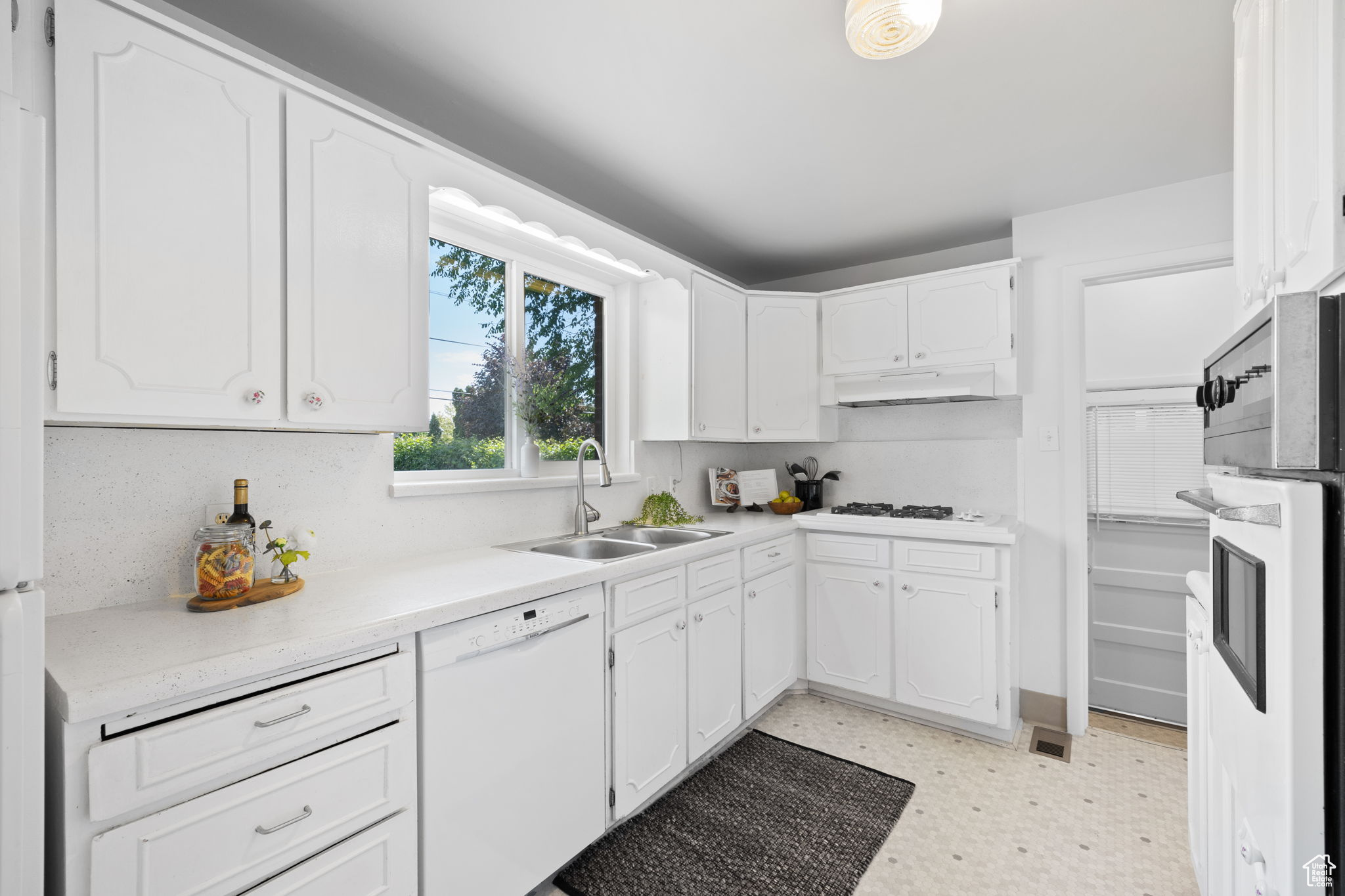 Kitchen featuring white appliances, sink, light tile flooring, and white cabinetry