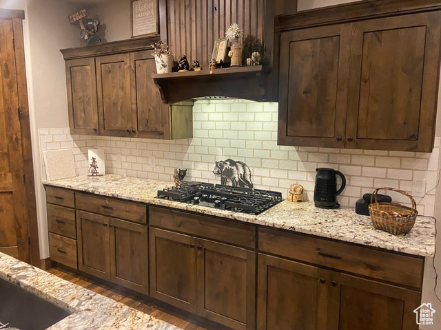 Kitchen with backsplash, dark wood-type flooring, dark brown cabinetry, and black gas stovetop