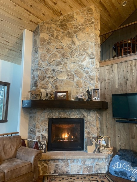 Living room featuring a stone fireplace, wood ceiling, and lofted ceiling