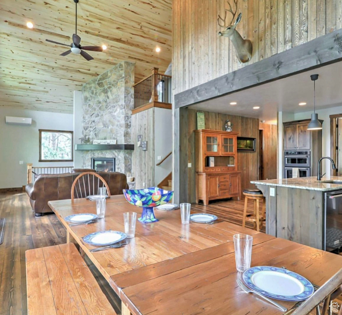 Dining room featuring dark hardwood / wood-style floors, wood walls, a stone fireplace, high vaulted ceiling, and sink