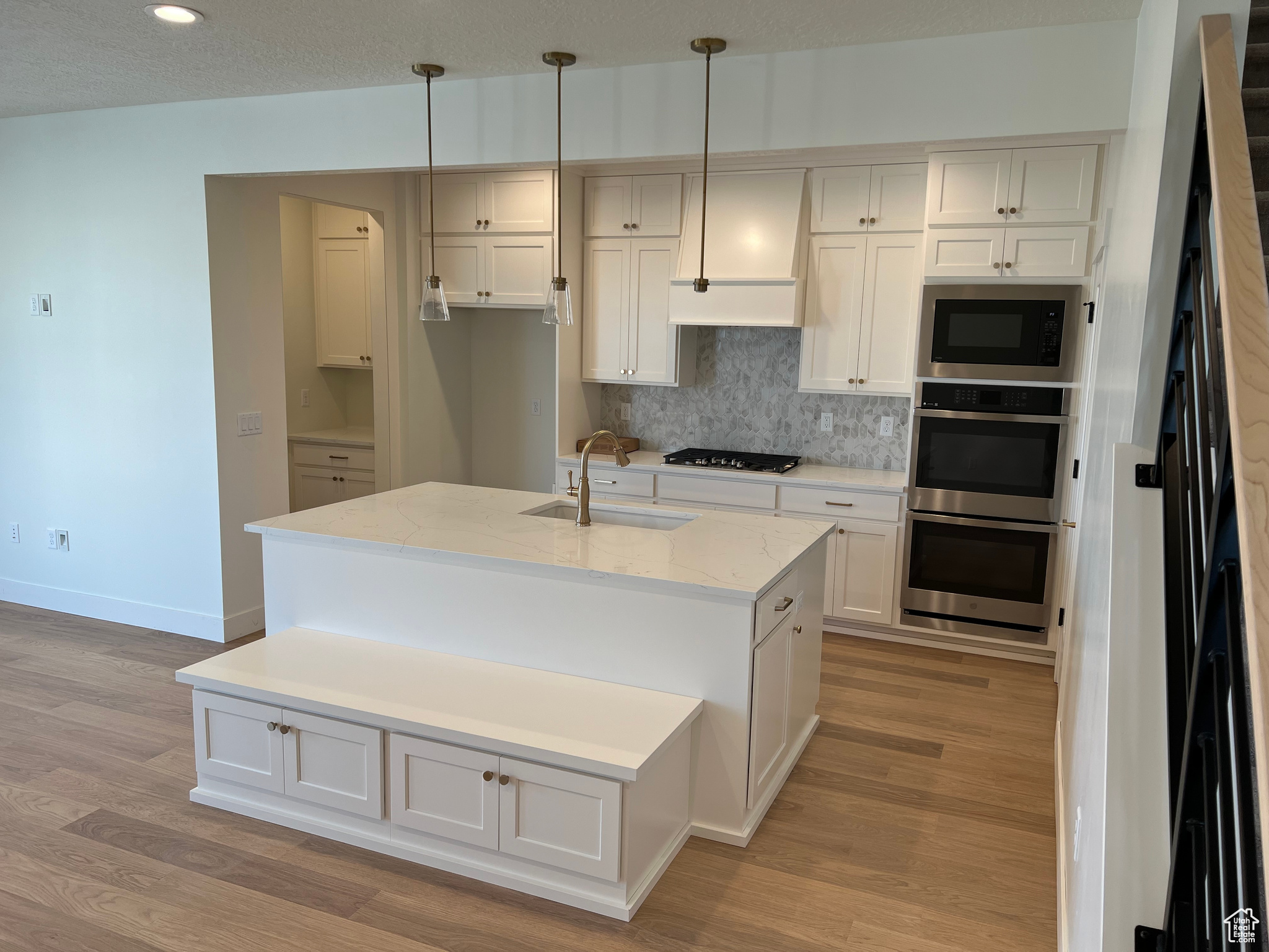 Kitchen featuring light stone counters, pendant lighting, light hardwood / wood-style flooring, a center island with sink, and sink