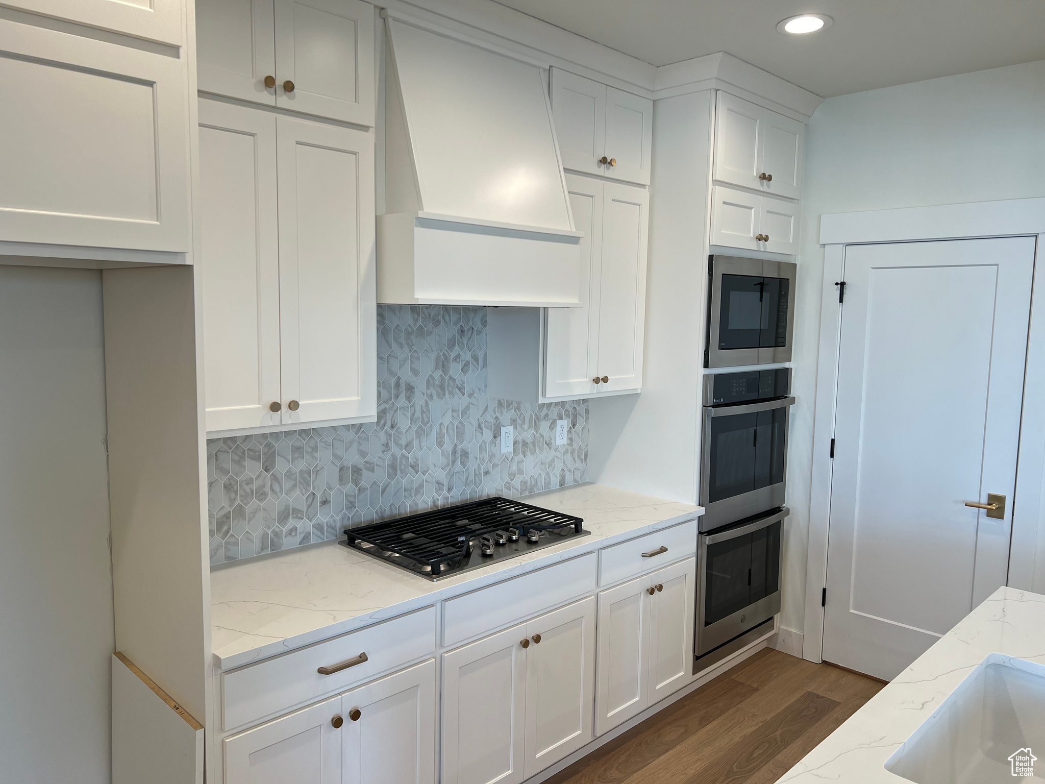 Kitchen featuring light stone countertops, white cabinetry, dark wood-type flooring, and premium range hood