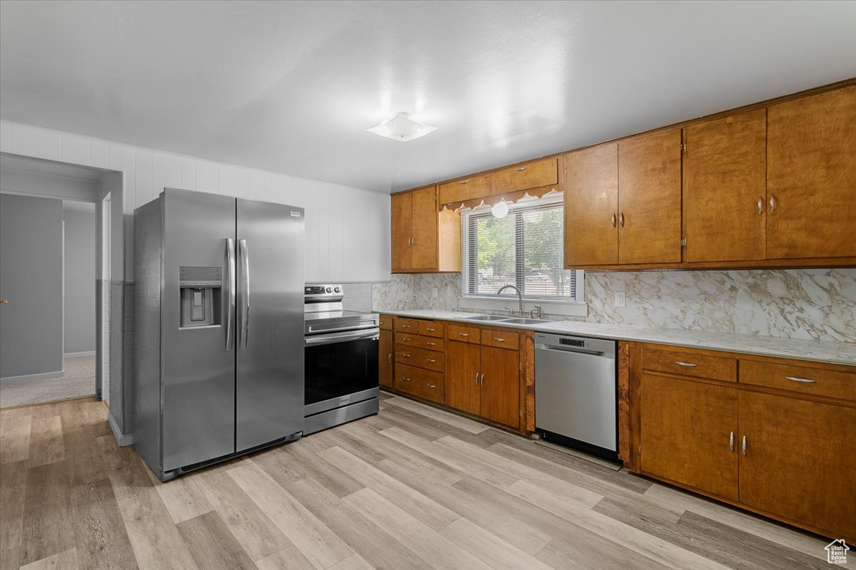 Kitchen with light hardwood / wood-style floors, appliances with stainless steel finishes, decorative backsplash, and sink