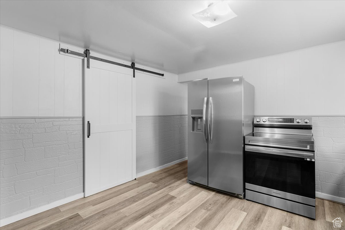 Kitchen featuring appliances with stainless steel finishes, light wood-type flooring, white cabinets, and a barn door